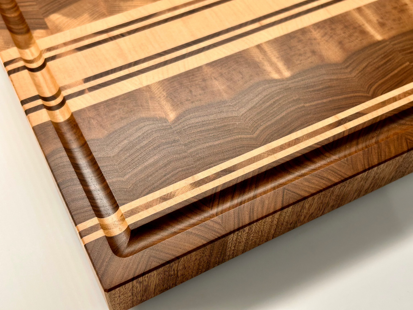 Détail du coin et de la rigole à jus sur une planche à dédouper en noyer français et érable, finition haut de gamme et fabriquée en France