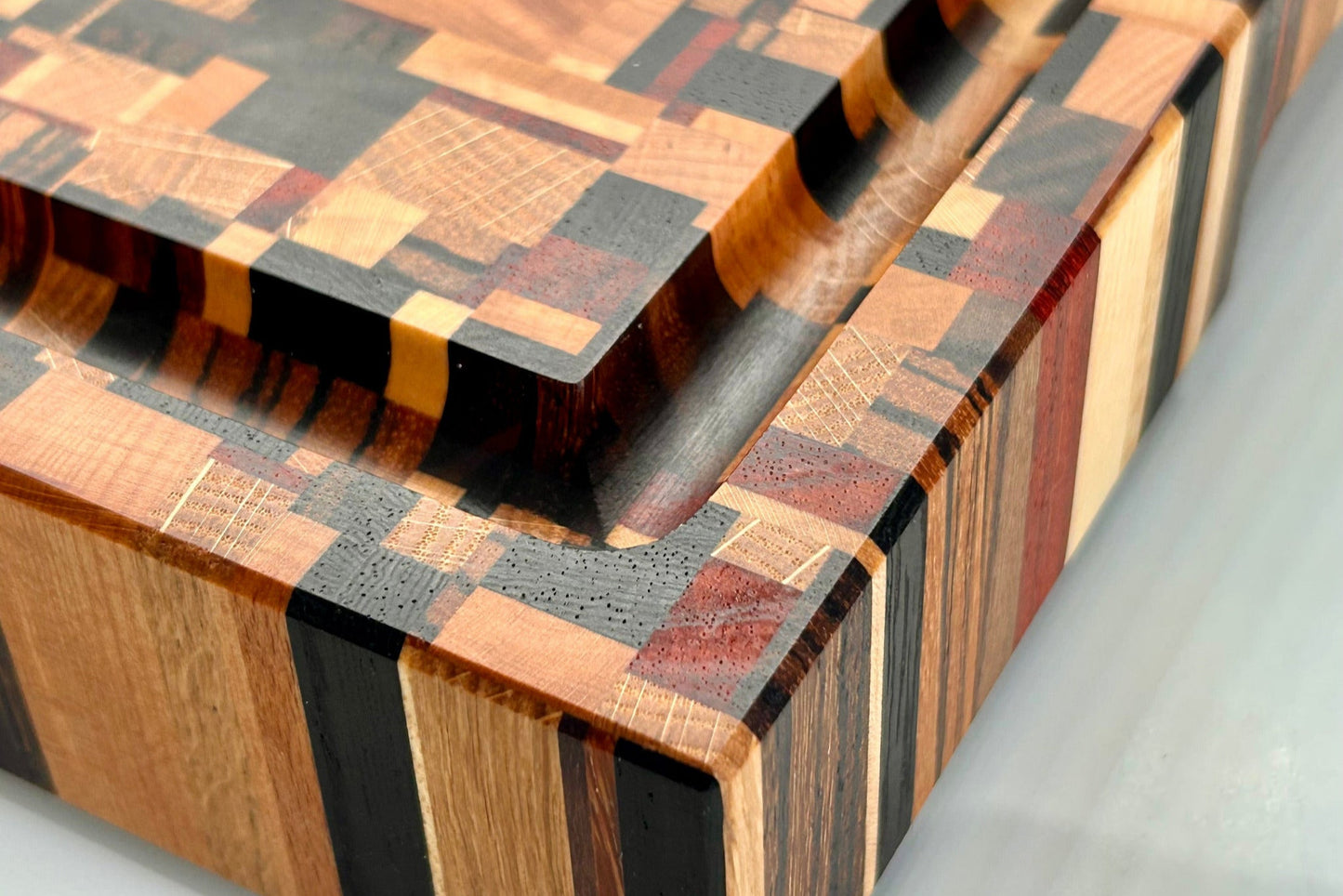 Gros plan sur un coin de la planche à découper artisanale en bois de bout avec rigole à jus, composée de 9 essences nobles.