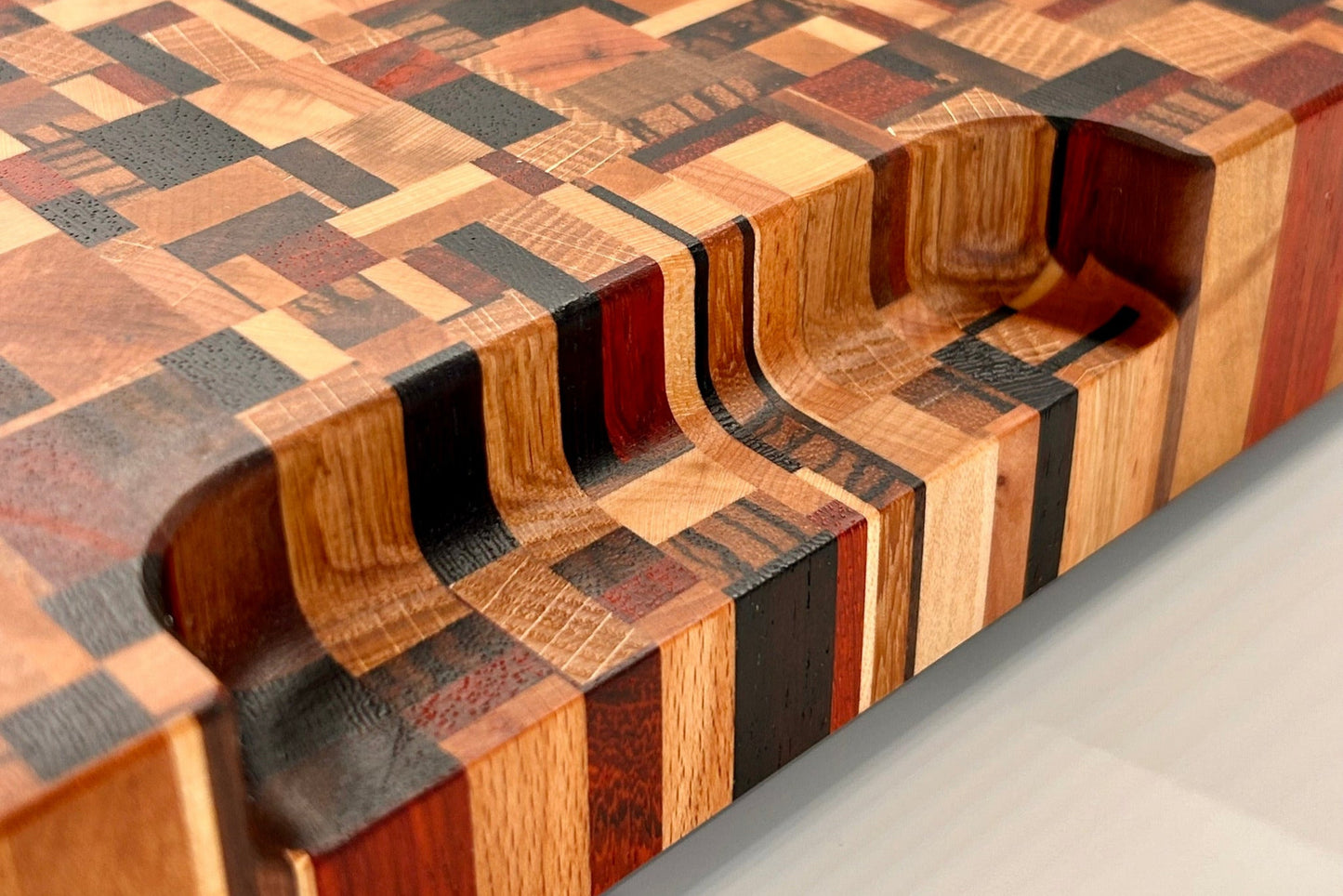Détail de la poignée intégrée d’une planche artisanale en bois de bout, composée de 9 essences nobles, finition haut de gamme.