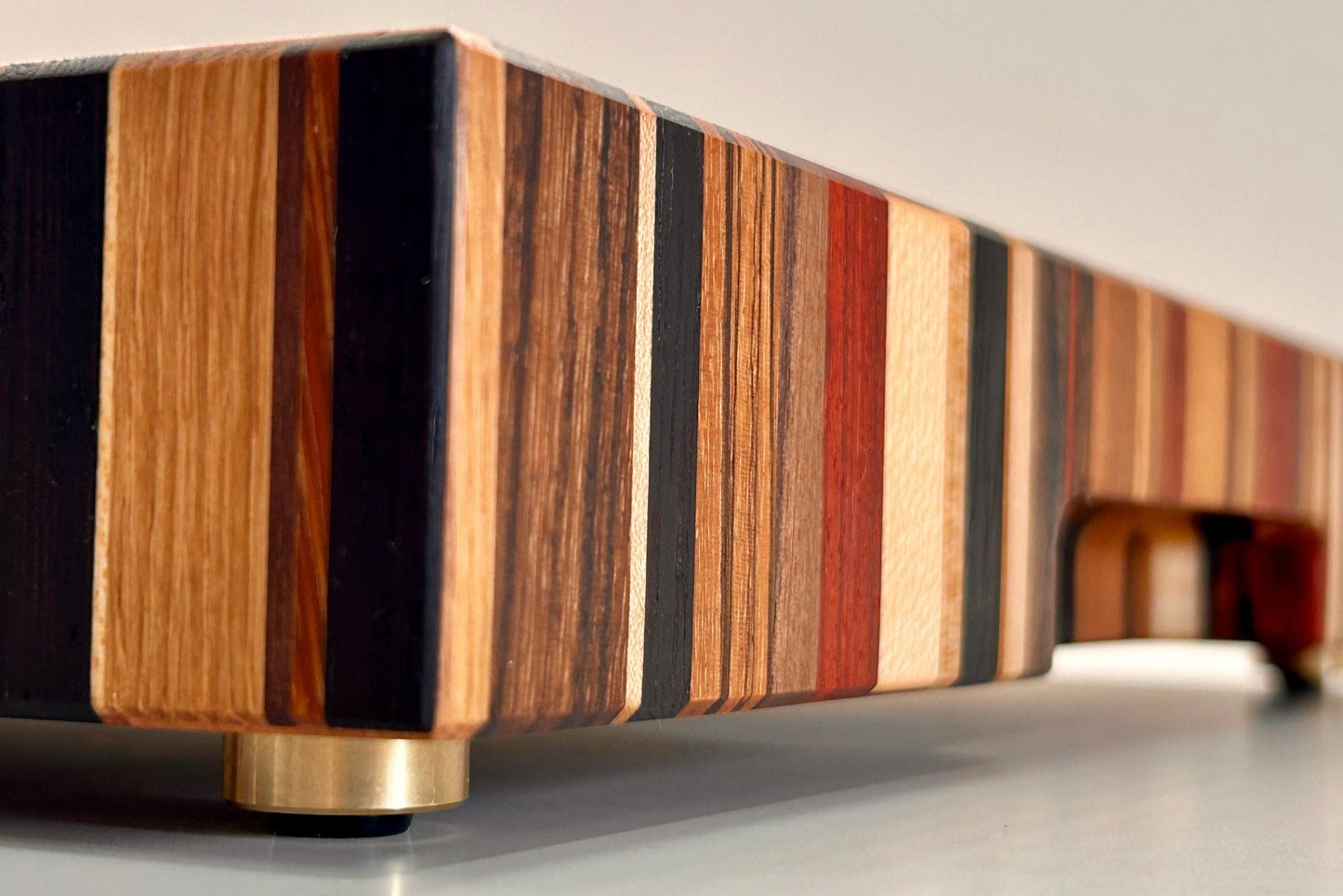 Gros plan sur la tranche et le pied en laiton massif fabriqué en France, sur une planche artisanale en bois de bout composée de 9 essences nobles.
