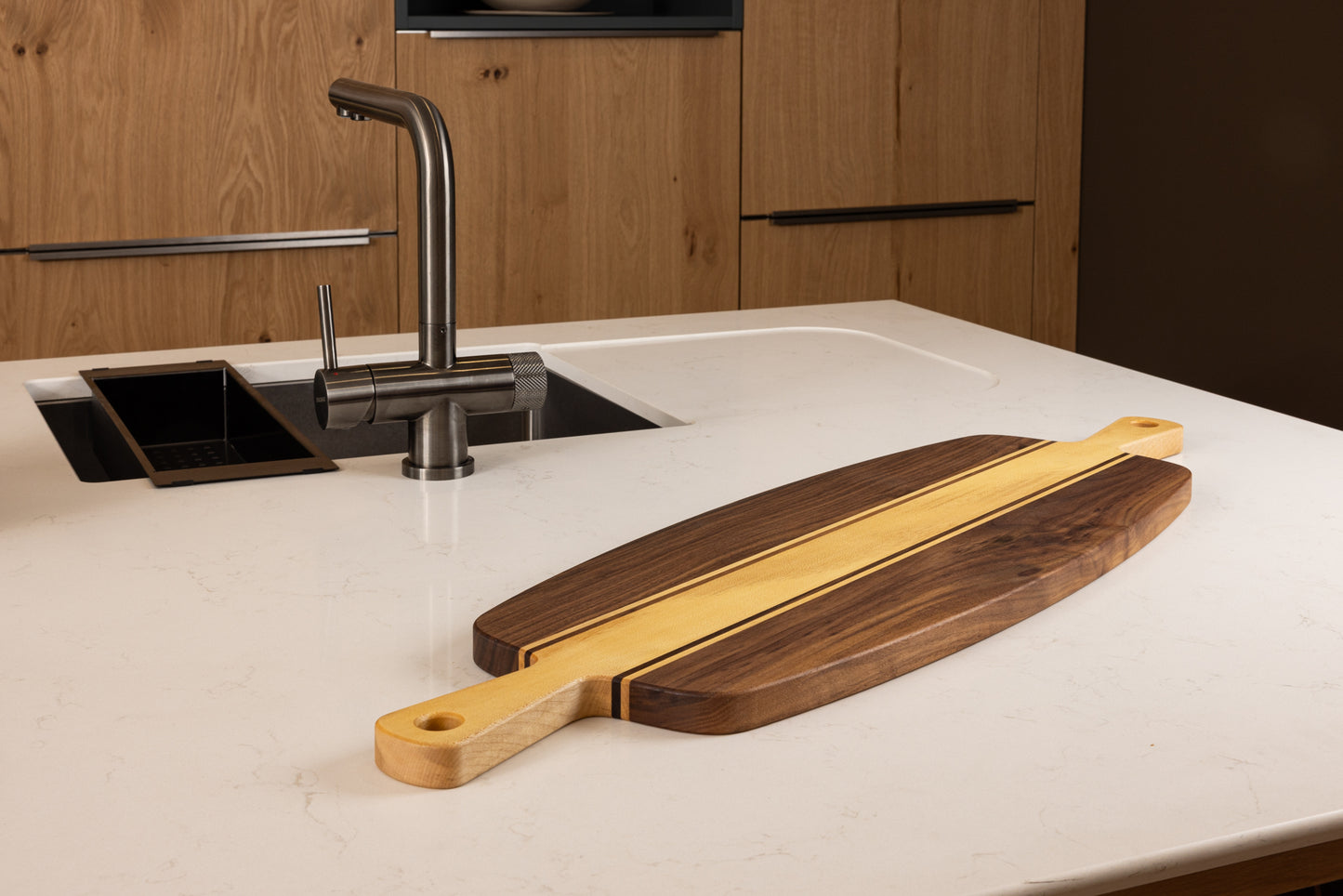 Planche apéro en bois massif noyer et érable avec double poignée, posée sur un plan de travail clair dans une cuisine contemporaine en bois