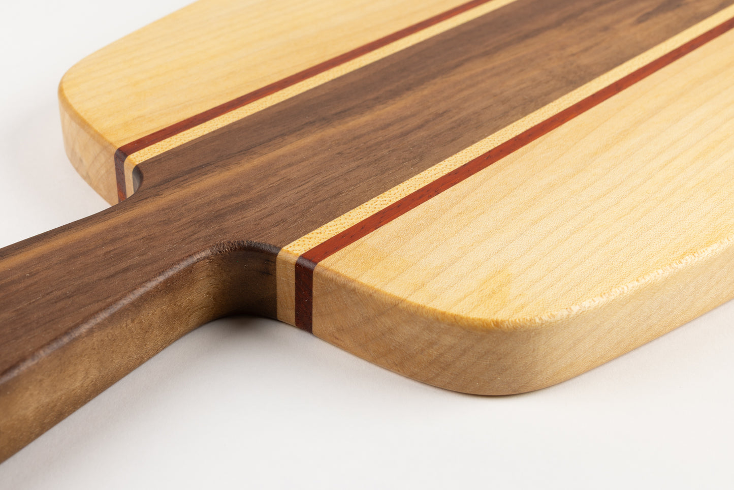 Gros plan sur l’assemblage des essences de bois de la planche apéro : poignée en noyer, filets de padouk et érable, avec finition huilée.