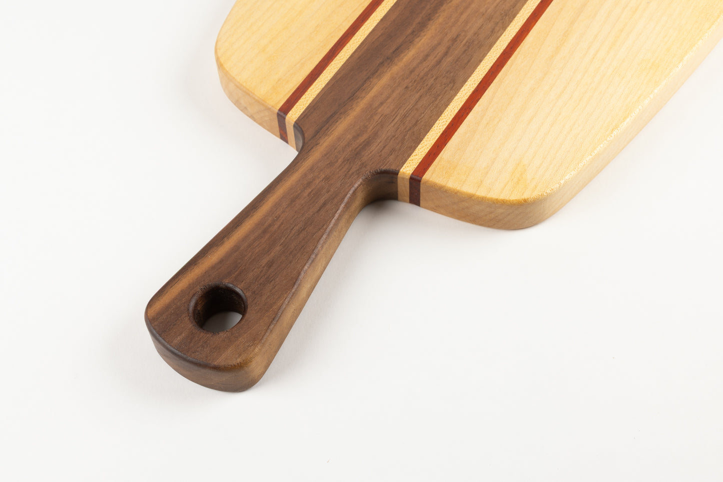Détail d’une planche apéro artisanale en bois massif avec poignée en noyer, filets de padouk et érable, finition huilée sur fond blanc.