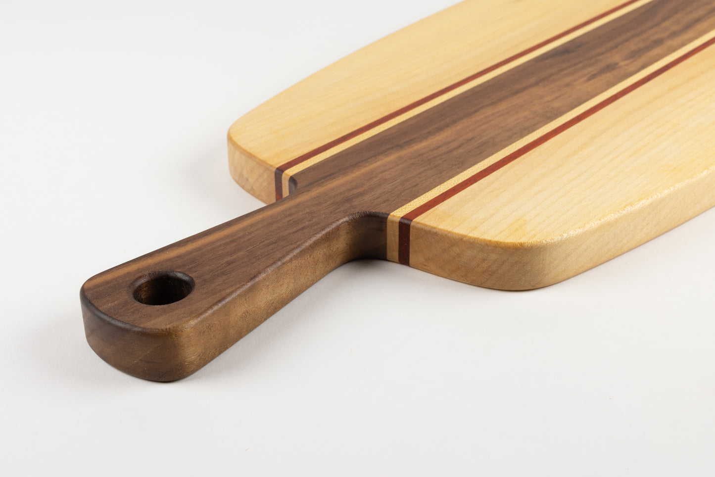 Gros plan sur la poignée d’une planche apéro artisanale en bois massif, associant noyer, érable et padouk