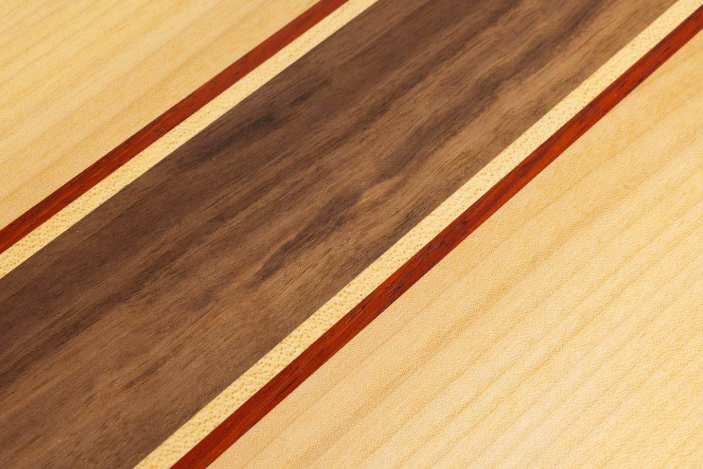 Gros plan sur les essences de bois utilisées pour une planche apéro : noyer, érable et padouk, avec finition huilée mettant en valeur le veinage.