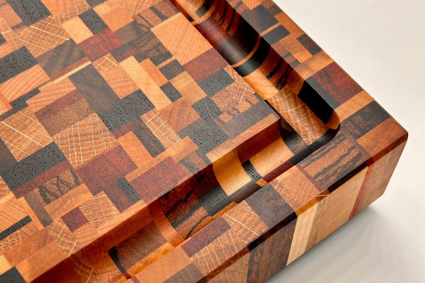 Détail de la rigole à jus profonde sur une planche à découper artisanale en bois de bout composée de 9 essences nobles.
