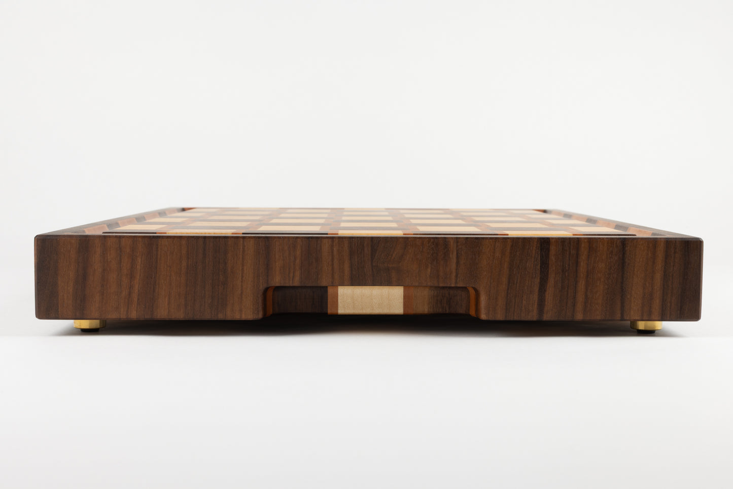 Vue détaillée d’une planche à découper artisanale de luxe en bois de bout, tranche en noyer au veinage marqué, poignée fraisée avec érable et poirier, finition élégante avec pieds en laiton.