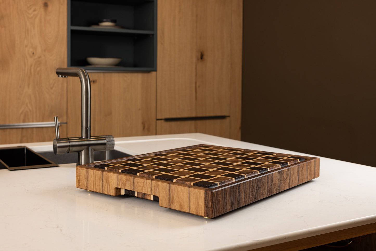 Vue latérale de la planche à découper Berlioz en wengé, noyer et érable, sur un plan de travail de cuisine moderne. Bois de bout précieux, finitions soignées et design graphique, fabrication artisanale française