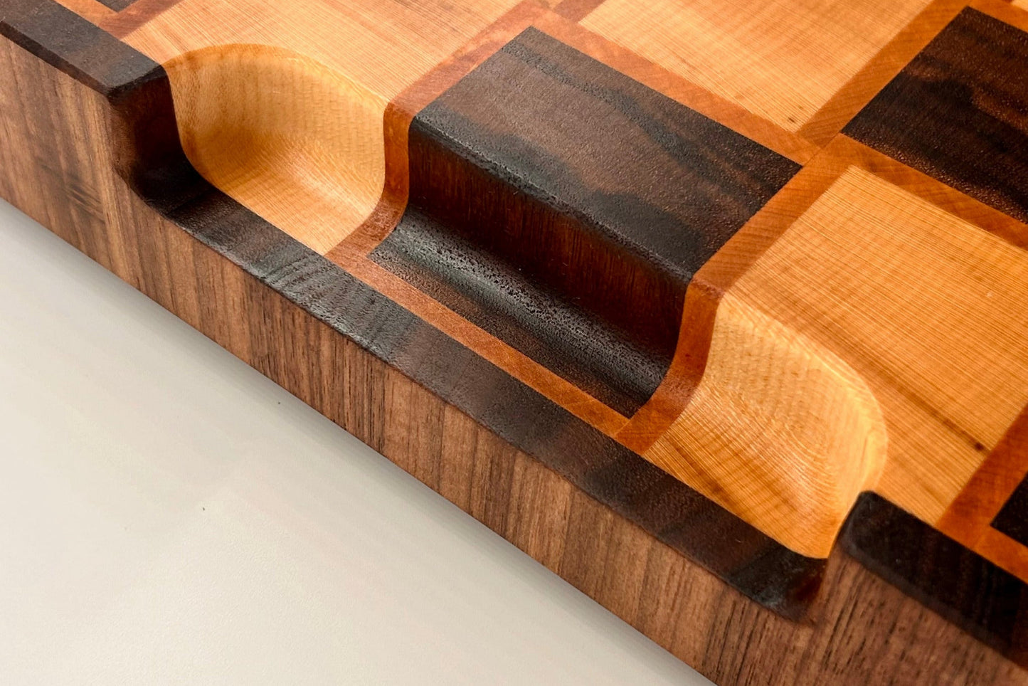 Détail de la poignée aux courbes douces de la planche à découper artisanale Berlioz en bois de bout, réalisée en noyer, érable et poirier.
