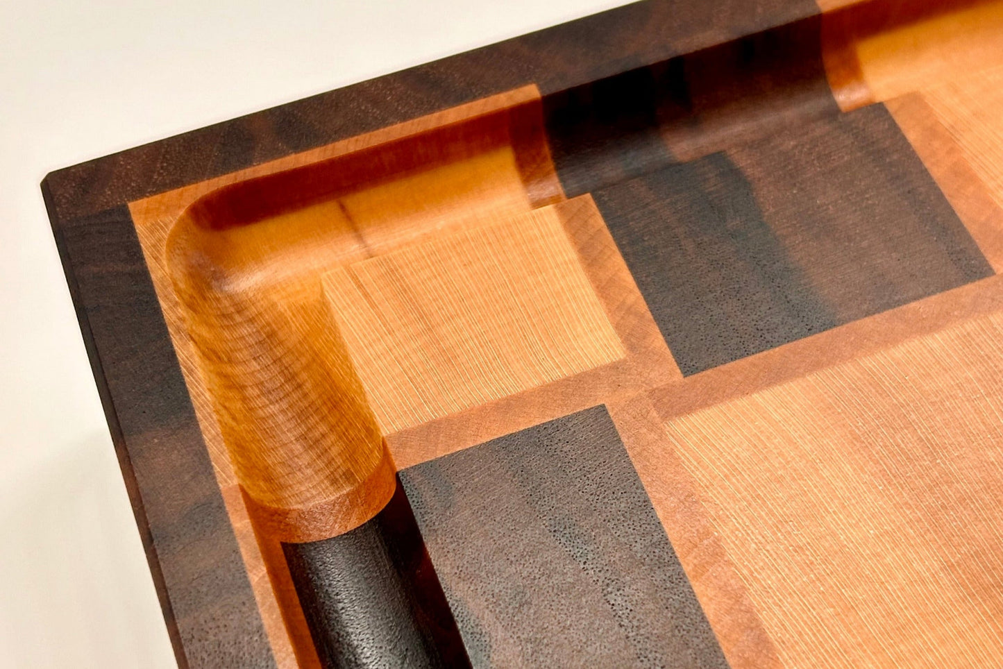 Détail de la rigole sur une planche à découper artisanale Berlioz avec un motif tissé Basketweave, réalisée en noyer, érable et poirier, avec une finition haut de gamme.