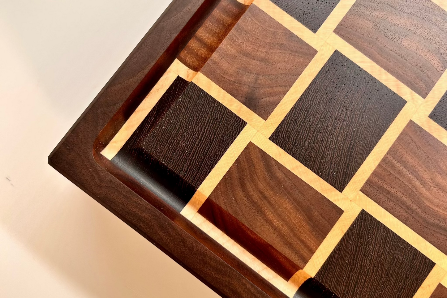 Gros plan en vue de dessus sur la rigole à jus d'une planche à découper artisanale en bois de bout, fabriquée avec soin en noyer américain, wengé et érable clair, mettant en valeur la précision des finitions