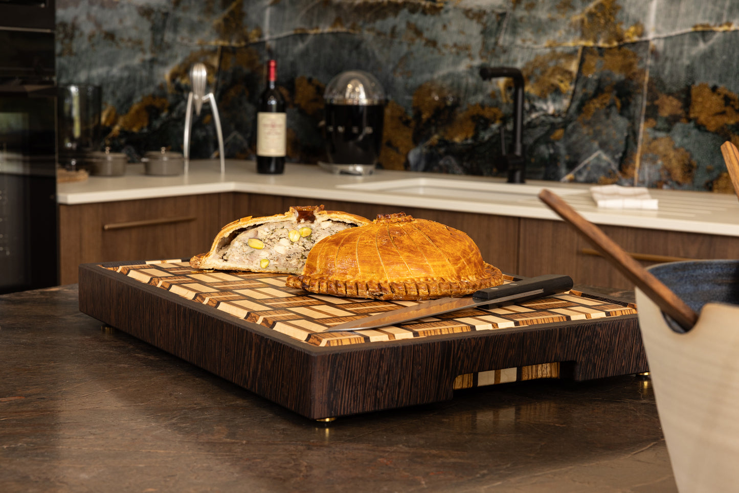 Planche en bois de bout haut de gamme en zebrano, noyer et érable utilisée comme support de découpe dans une cuisine élégante, avec une tourte faite maison et un couteau de chef