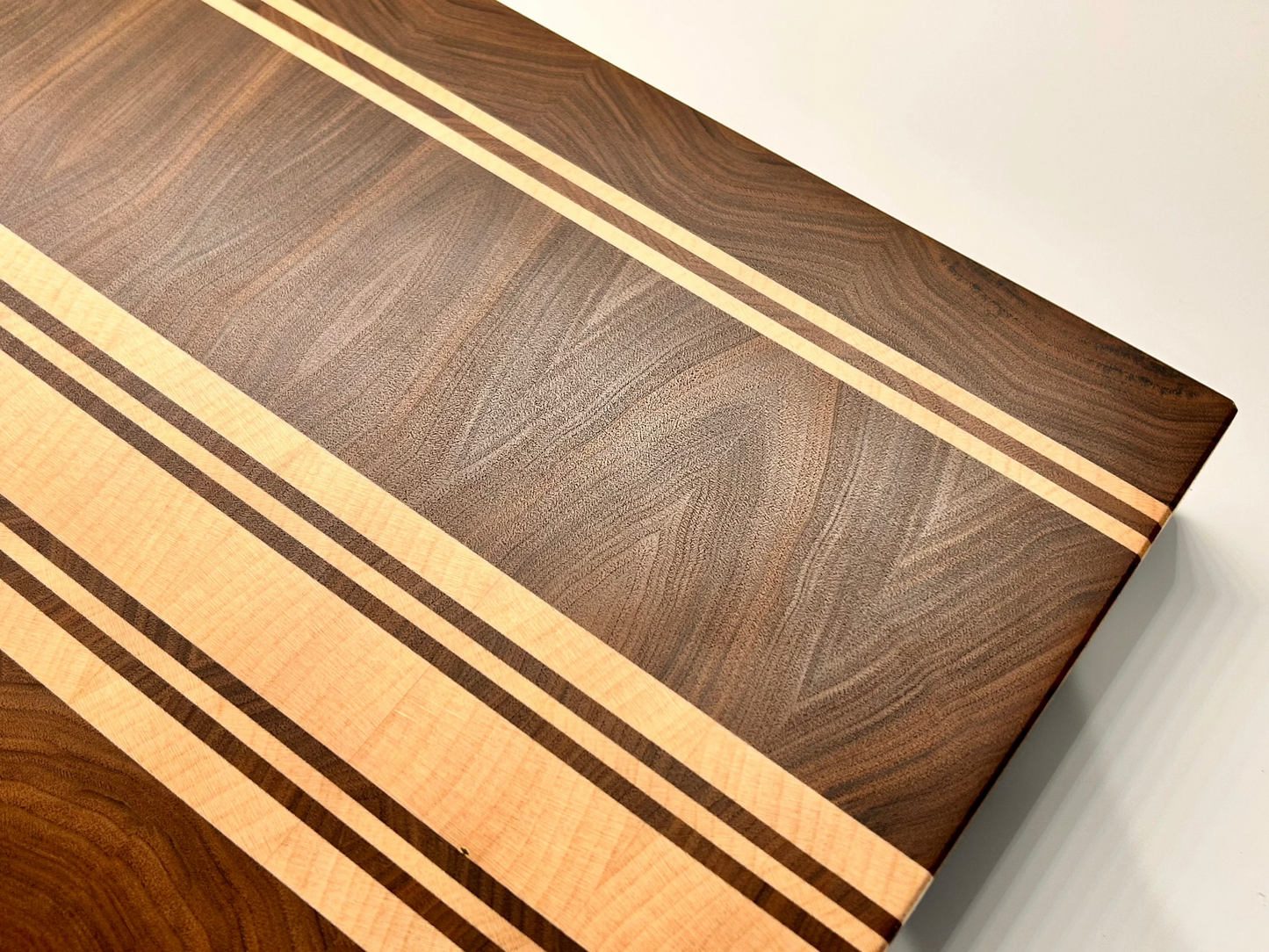 Vue du dessus sur le coin d'une planche à découper artisanale en noyer français et érable, sans rigole à jus