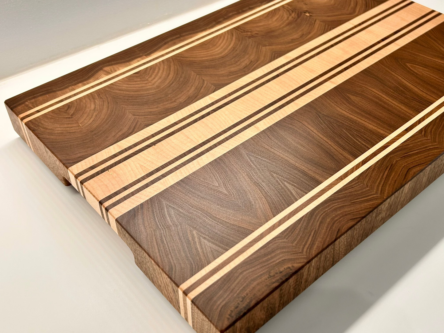 Vue de trois quart d'une planche à découper artisanale en noyer français et érable, surface finement poncée et lustrée, sans rigole à jus