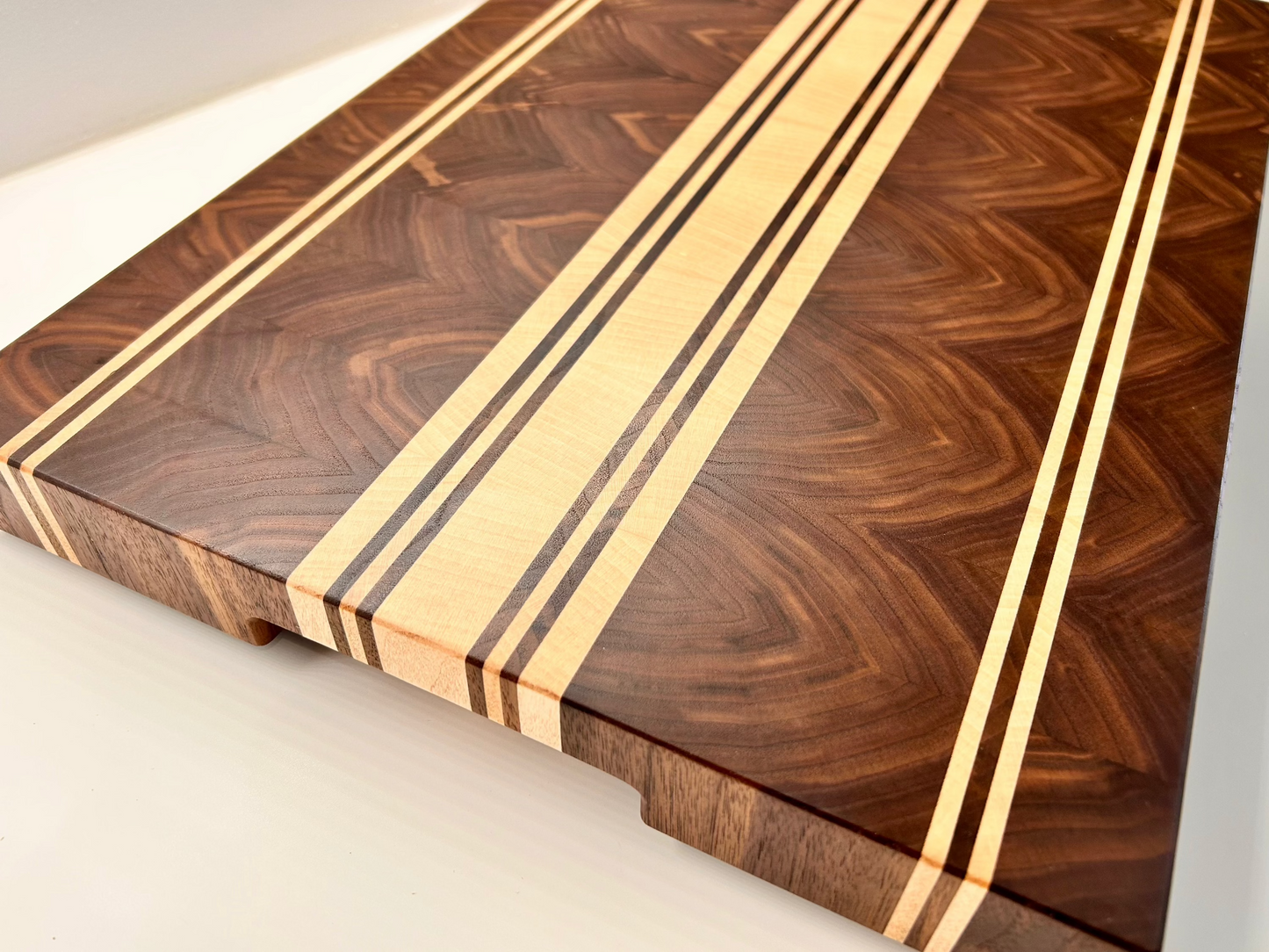 Vue de coté sur une planche à découper artisanale en noyer américain et érable, sans rigole à jus