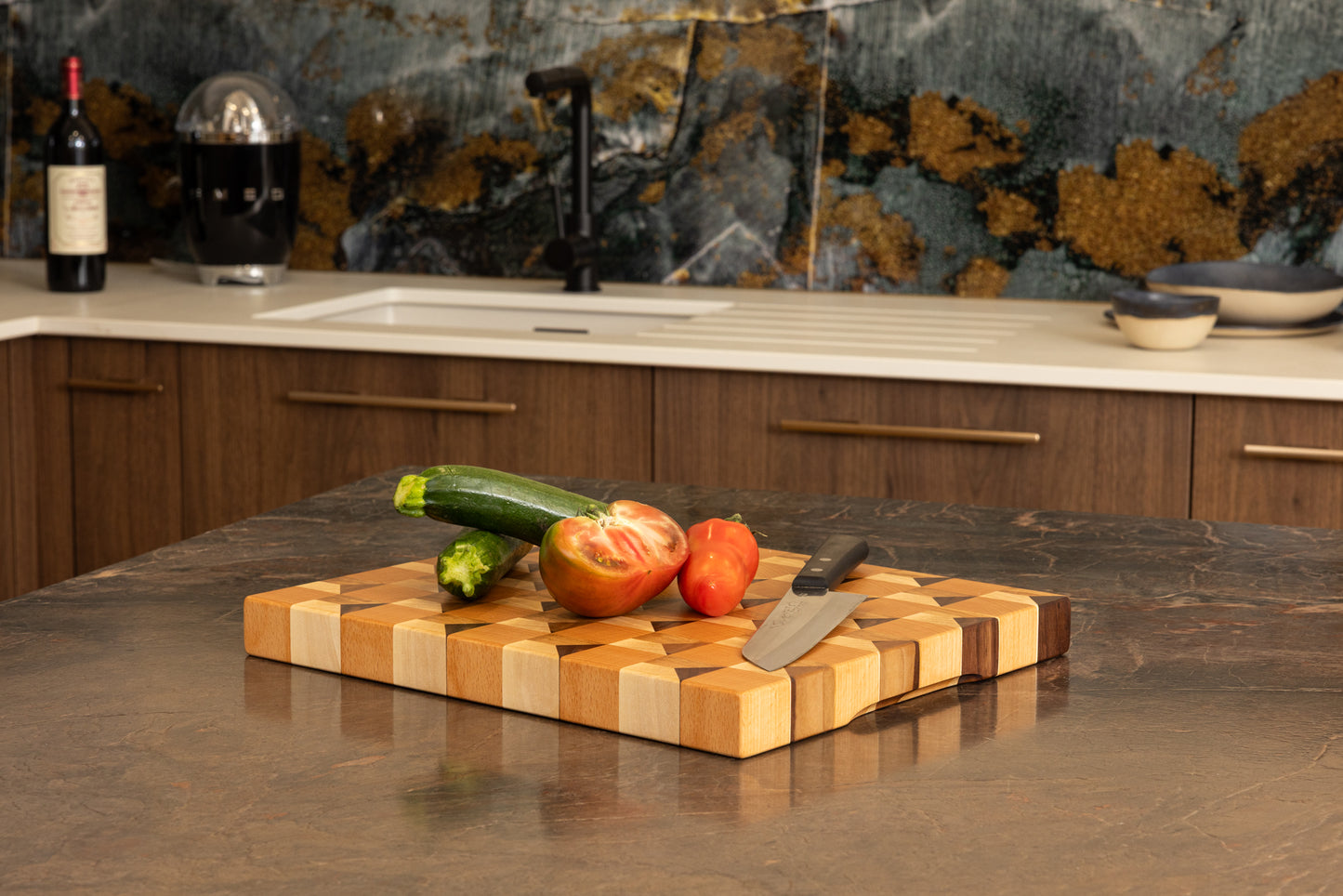 Planche à découper artisanale trompe l’œil, illusion de cubes en relief, bois de bout multi-essences sur un plan de travail sombre en granit, légumes frais et couteau de chef, Made in France