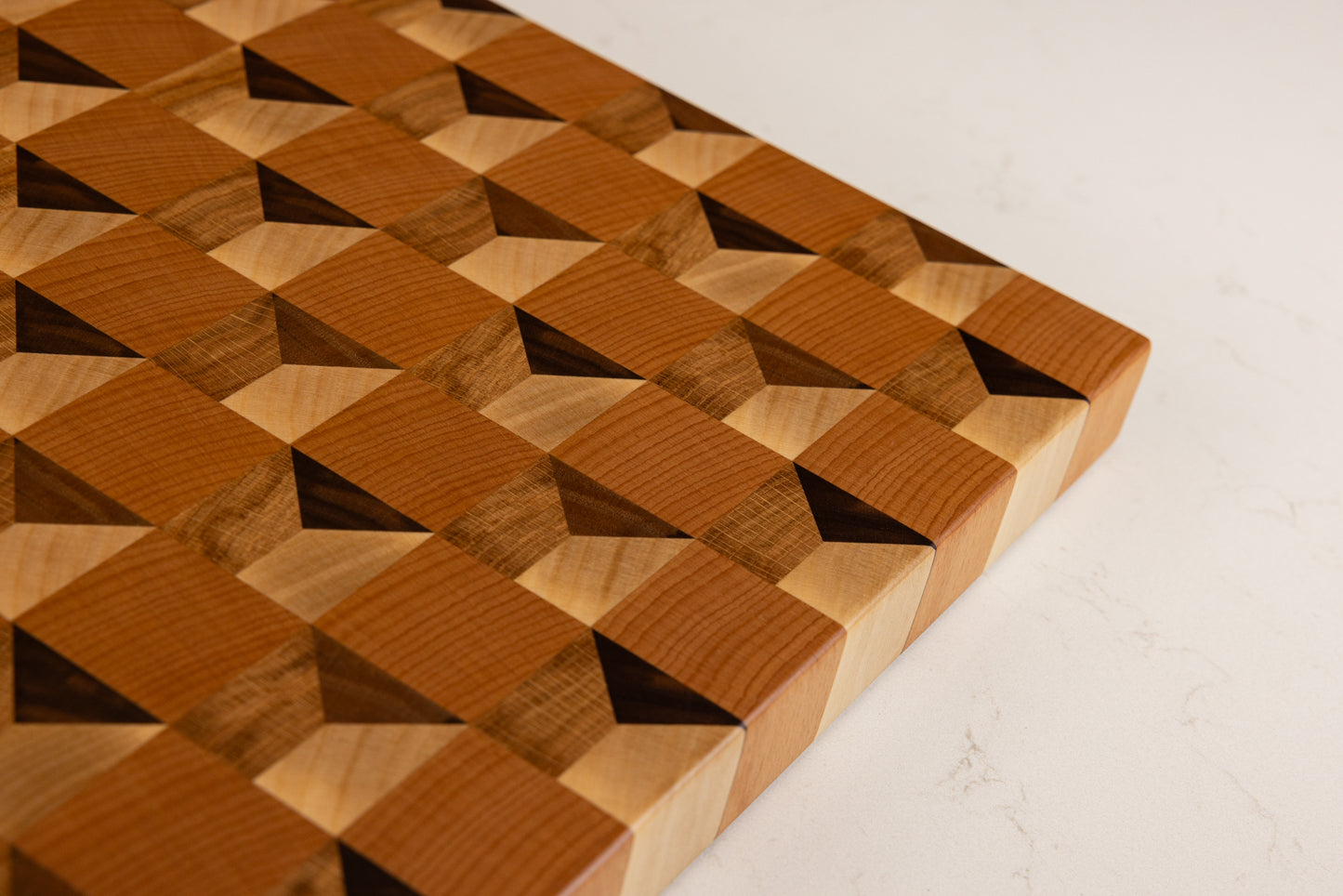 Vue de dessus incliné de la planche à découper Cube, révélant l’effet trompe-l’œil cubique saisissant, réalisée en bois de bout multi-essences, artisanat français haut de gamme.