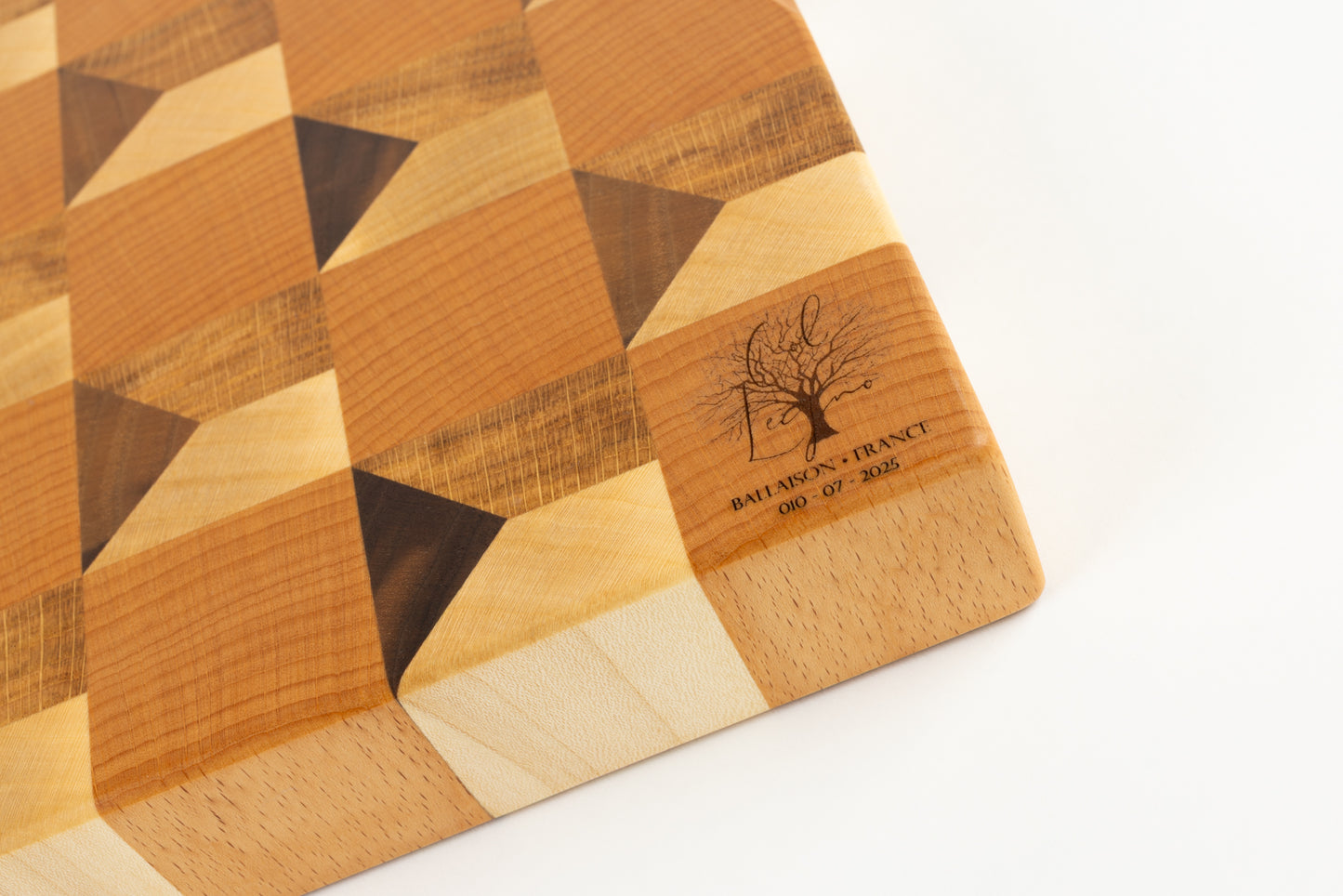 Planche à découper Cube, vue du coin avec logo gravé, motif trompe-l’œil cubique en chêne français, érable, hêtre et noyer américain, pièce de luxe Made in France.