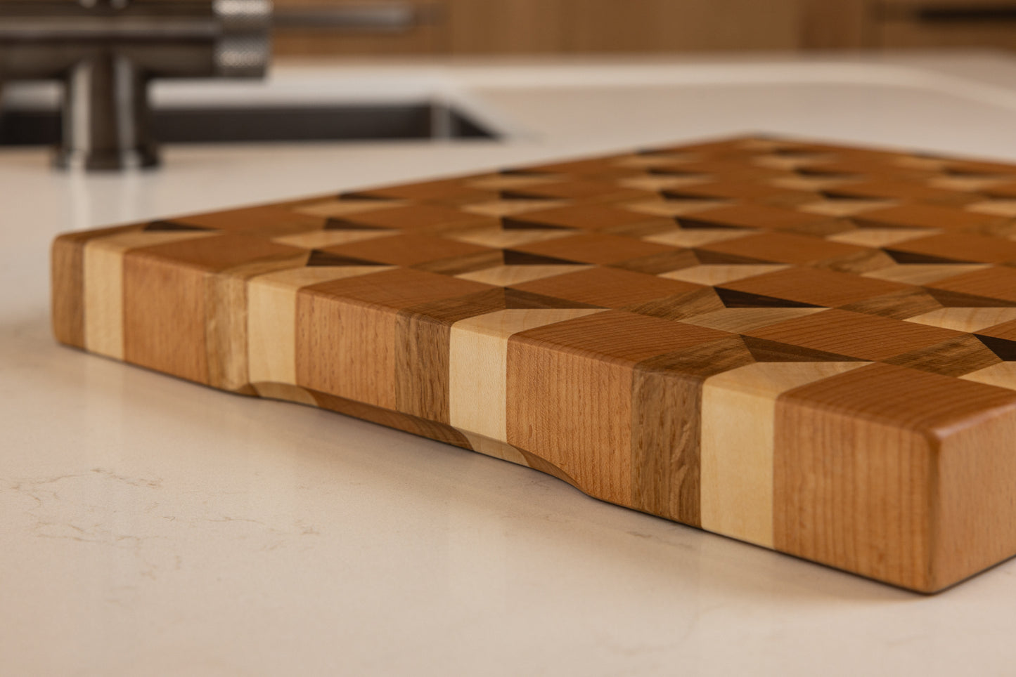 Vue du coin de la planche à découper Cube, bords arrondis et lustrés, design cubique trompe-l’œil en bois noble multi-essences, posée dans une cuisine moderne en chêne.