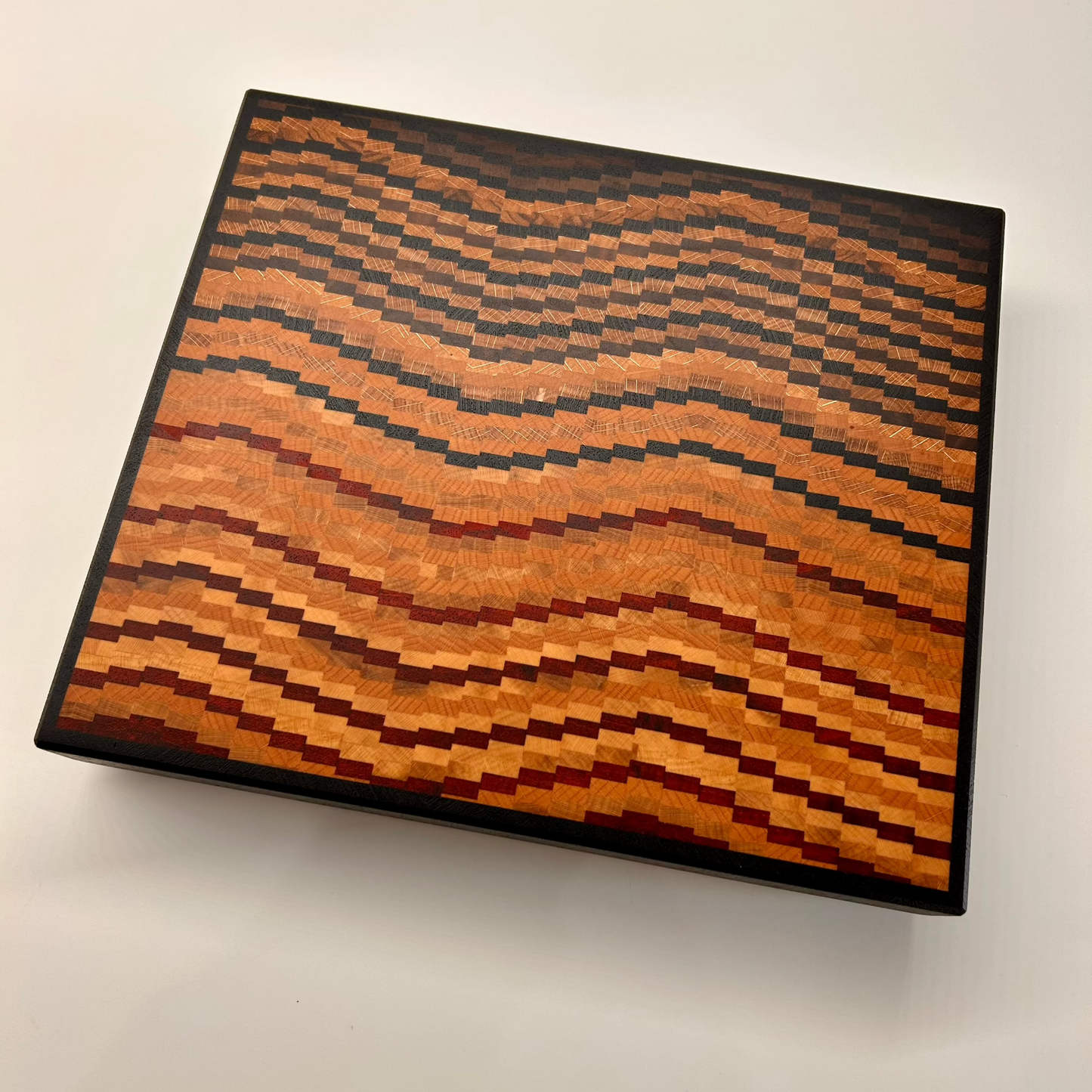 Planche à découper artisanale en bois massif multi-essences. Design graphique, moderne et haut de gamme, fabriquée en Haute-Savoie.