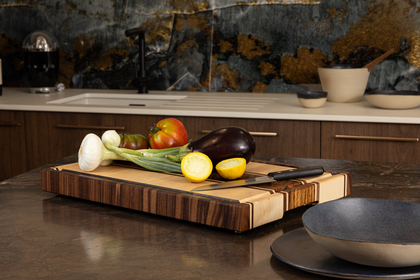 Planche à découper en bois massif fabriquée artisanalement, modèle Couperin en zebrano, érable et noyer américain, utilisée pour la préparation de légumes sur un plan de travail de cuisine moderne
