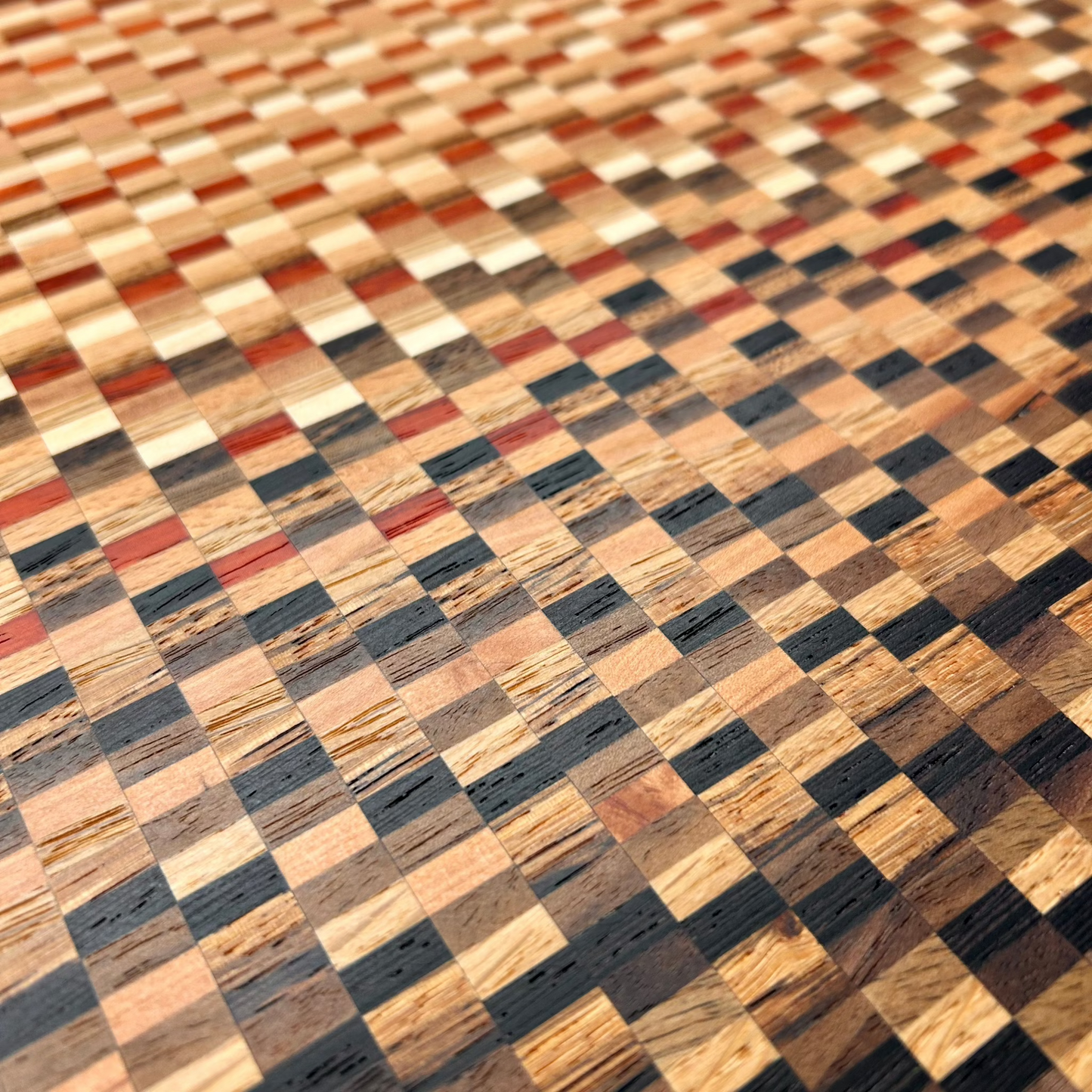 Gros plan sur le motif graphique d’une planche à découper artisanale en bois massif multi-essences. Design moderne et unique.