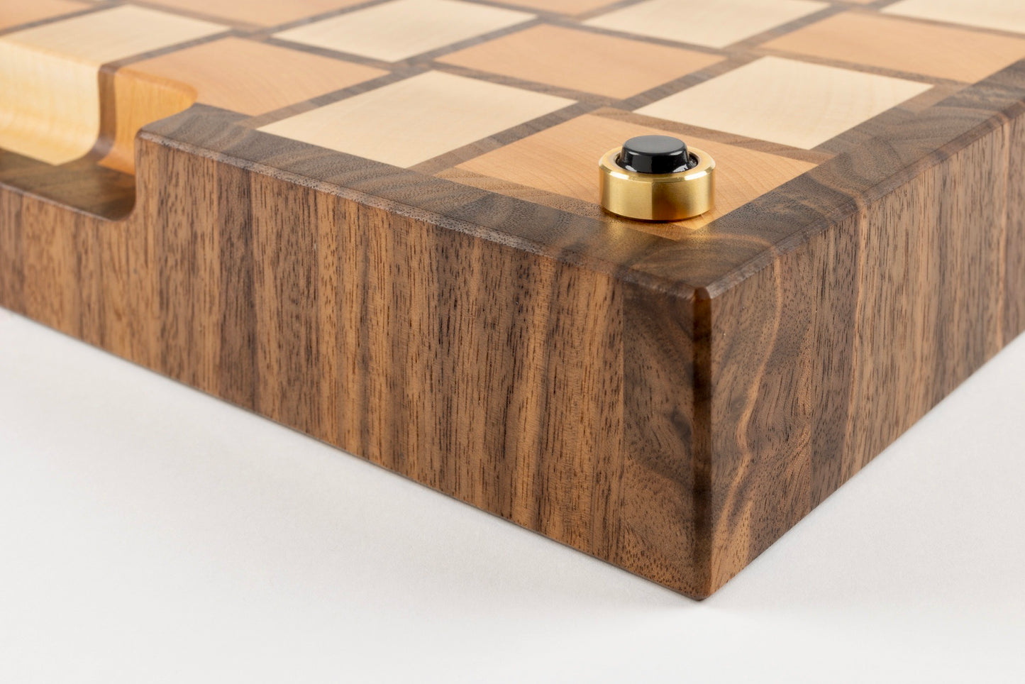 Gros plan sur le coin de la planche à découper Berlioz, motif damier tissé en érable, noyer américain et hêtre, détail du pied en laiton massif fabriqué en France avec patin antidérapant haut de gamme.