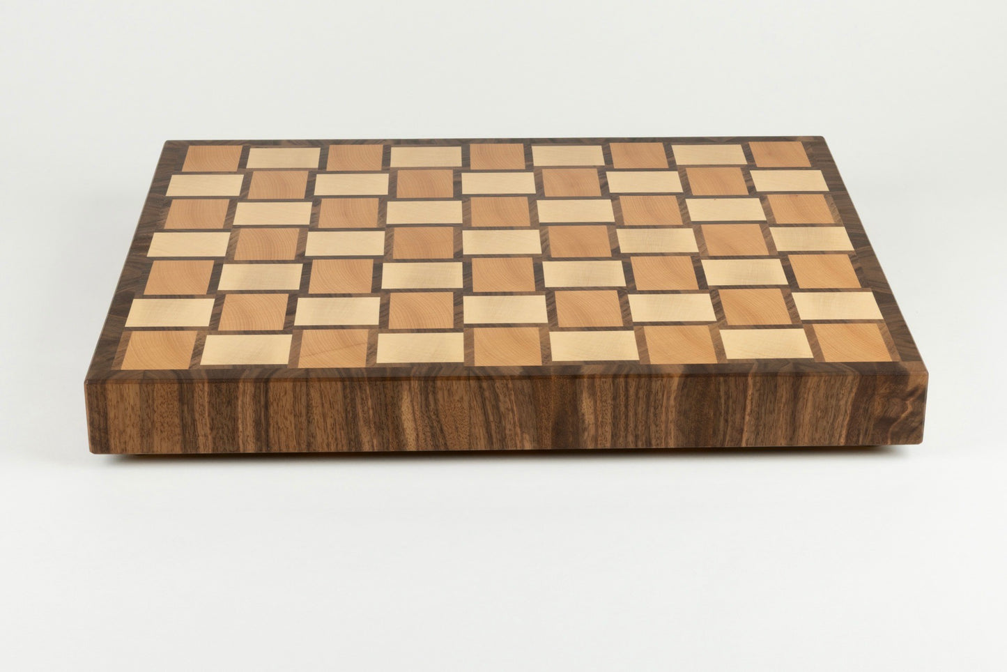 Vue de face de la planche à découper Berlioz, avec bordure élégante et son motif damier tissé en bois de bout, réalisée en érable, noyer américain et hêtre, pièce artisanale française haut de gamme.