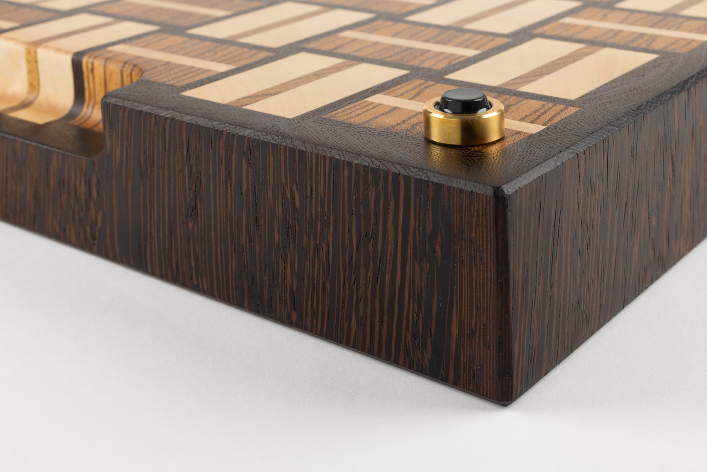 Planche à découper en bois de bout de luxe Berlioz, gros plan sur le coin et le pied en laiton massif fabriqué en France, patin antidérapant de qualité, motif damier tissé en wengé, zebrano et érable, fabrication artisanale haut de gamme.