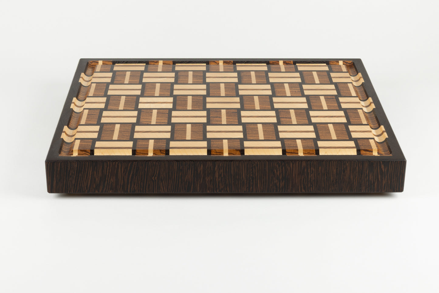 Planche à découper en bois de bout de luxe, modèle Berlioz. Vue de face mettant en valeur la bordure et le motif en damier tissé, essences nobles wengé, zebrano et érable, fabrication artisanale Made in France avec pieds en laiton massif.