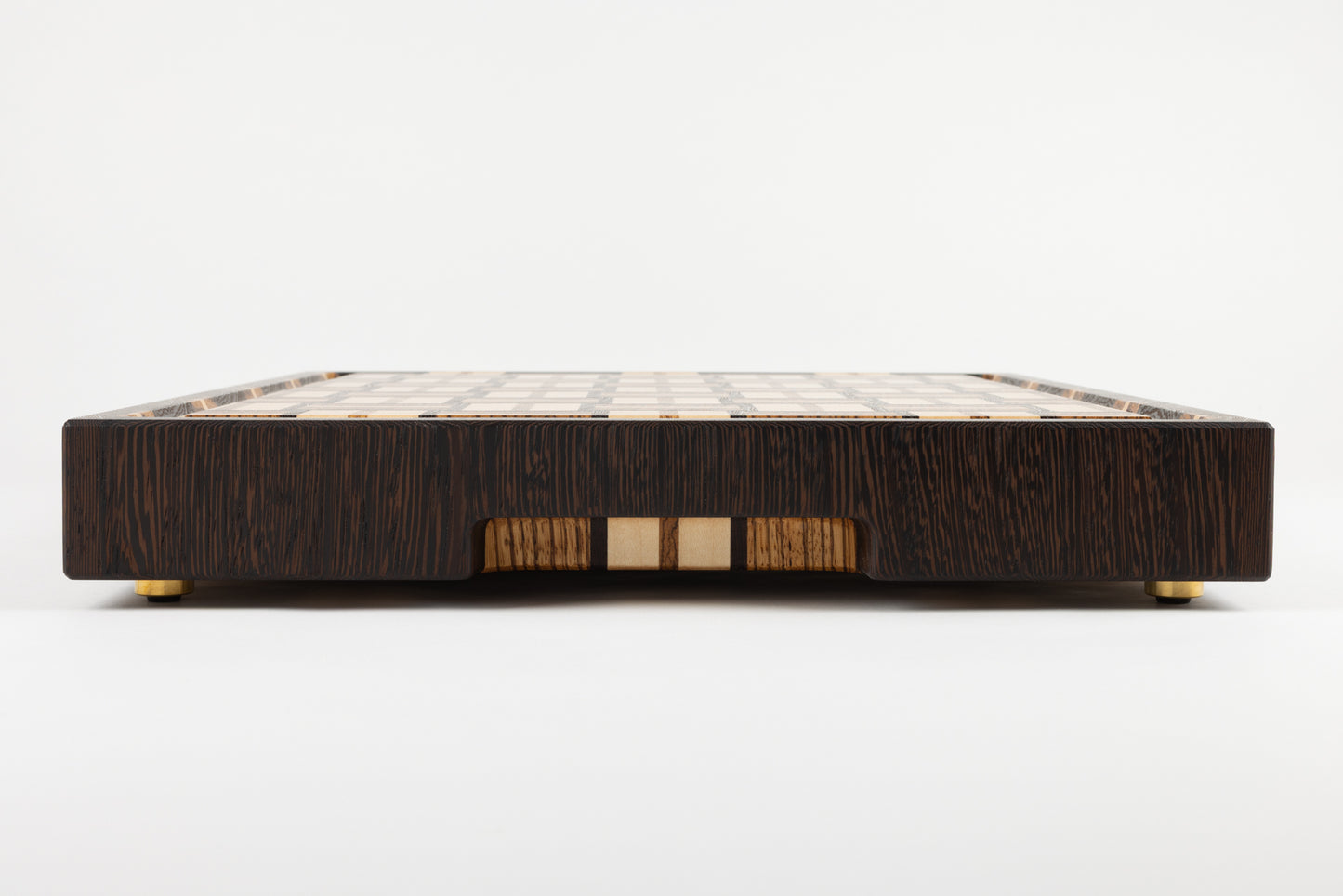 Vue latérale de la planche à découper en bois de bout artisanale Berlioz, avec poignée fraisée et pieds en laiton massif Made in France, motif damier tissé en wengé, zebrano et érable, finitions haut de gamme.
