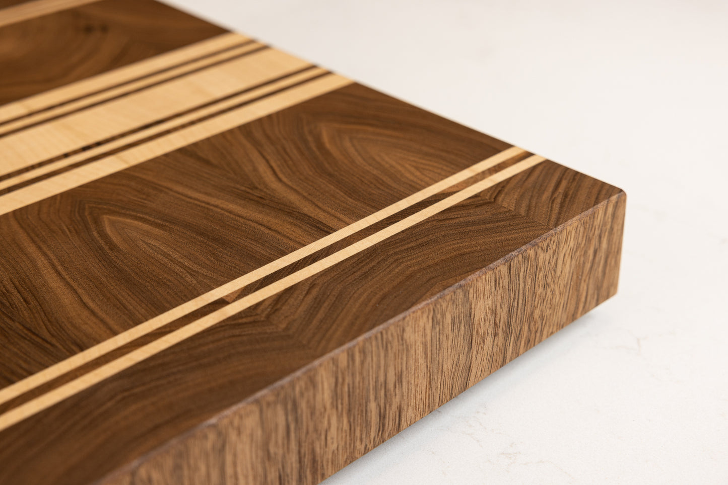 Vue de trois quarts du coin de la planche à découper artisanale Debussy en noyer français et érable, veinage élégant d'une grande finesse, finition haut de gamme Made in France.