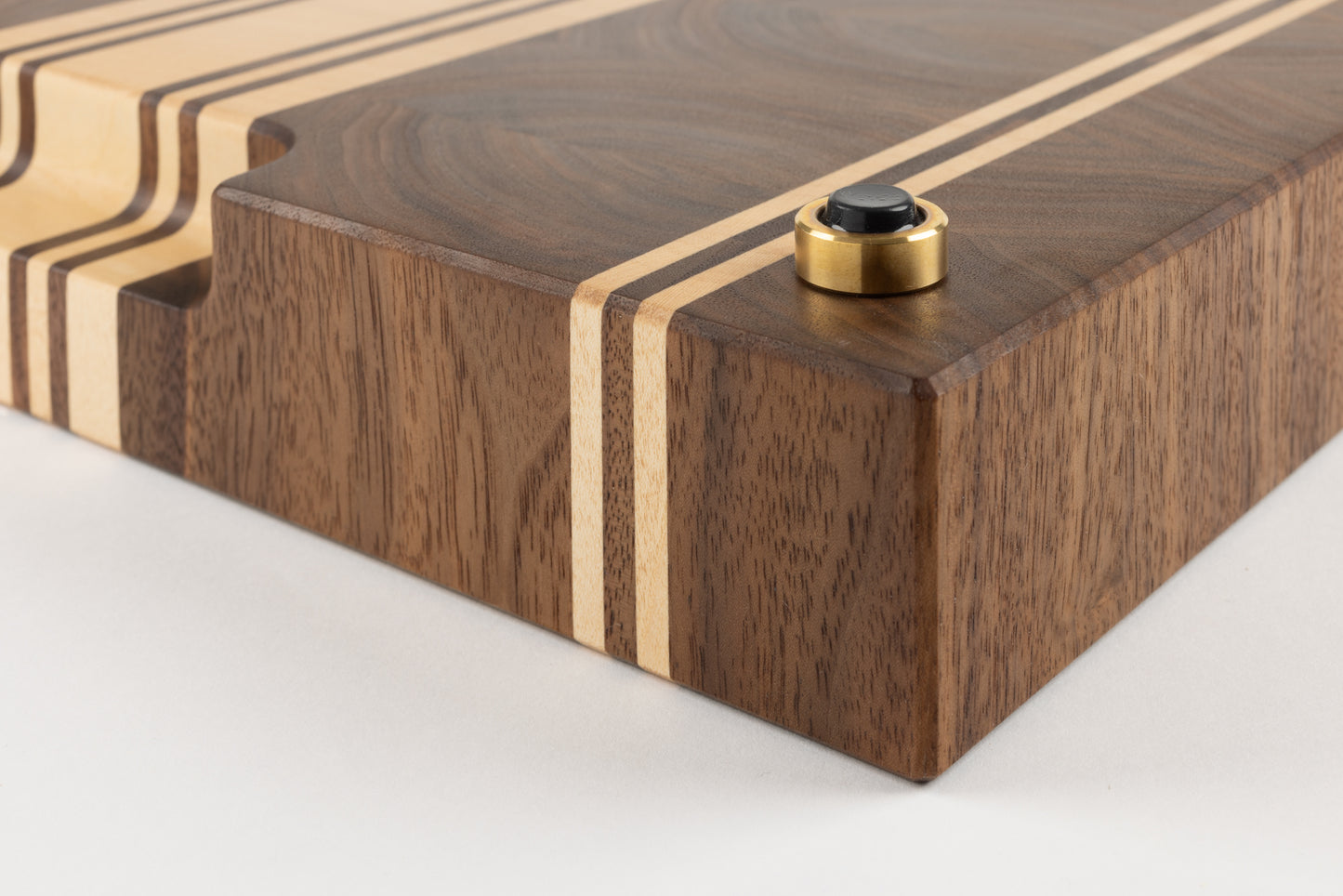 Vue du coin de la planche à découper artisanale Debussy, gros plan sur le pied en laiton massif Made in France, patin antidérapant et arêtes finement travaillées.