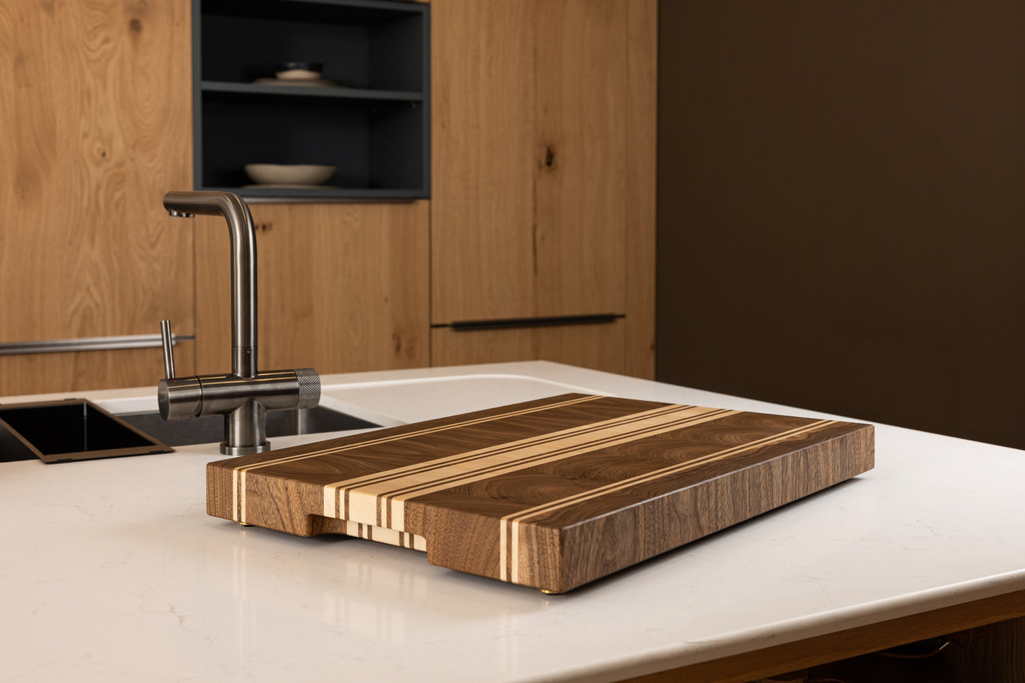 Vue générale de la planche à découper artisanale Debussy en noyer français et érable, posée sur un plan de travail dans une cuisine moderne en chêne haut de gamme.