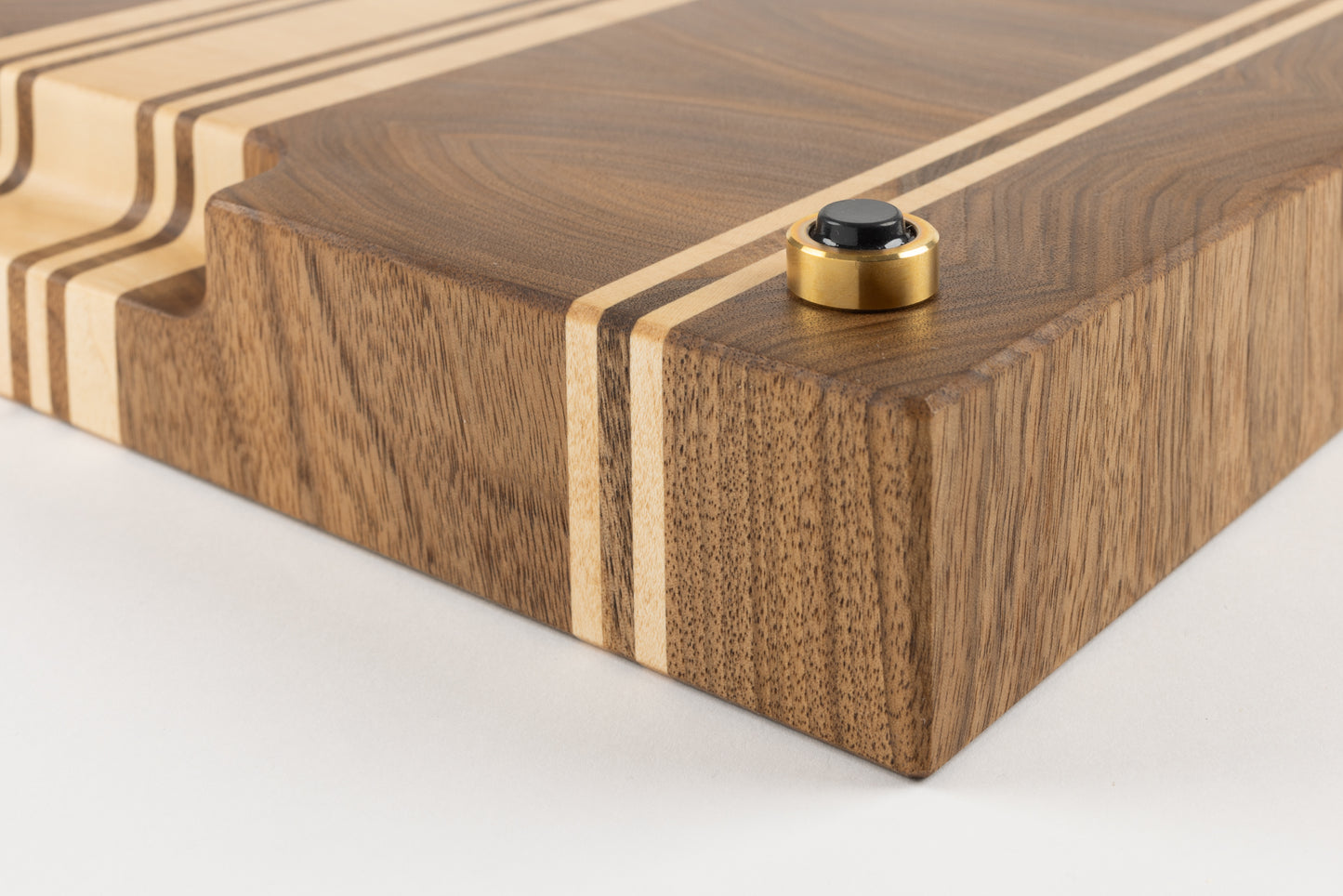 Planche à découper de luxe Debussy en noyer français et érable, détail du coin avec pied en laiton massif et patin antidérapant premium, veinage fin et élégant, fabrication artisanale française.