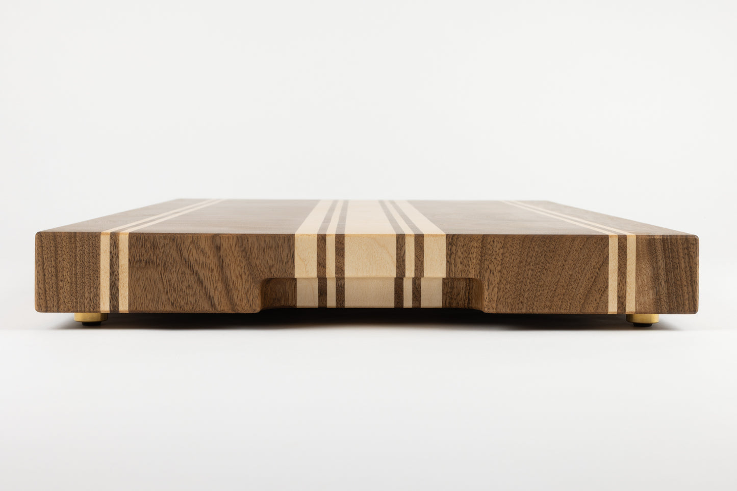 Vue latérale de la planche à découper artisanale Debussy en noyer français et érable, avec poignée fraisée élégante et pieds en laiton massif Made in France, veinage raffiné et finitions haut de gamme.