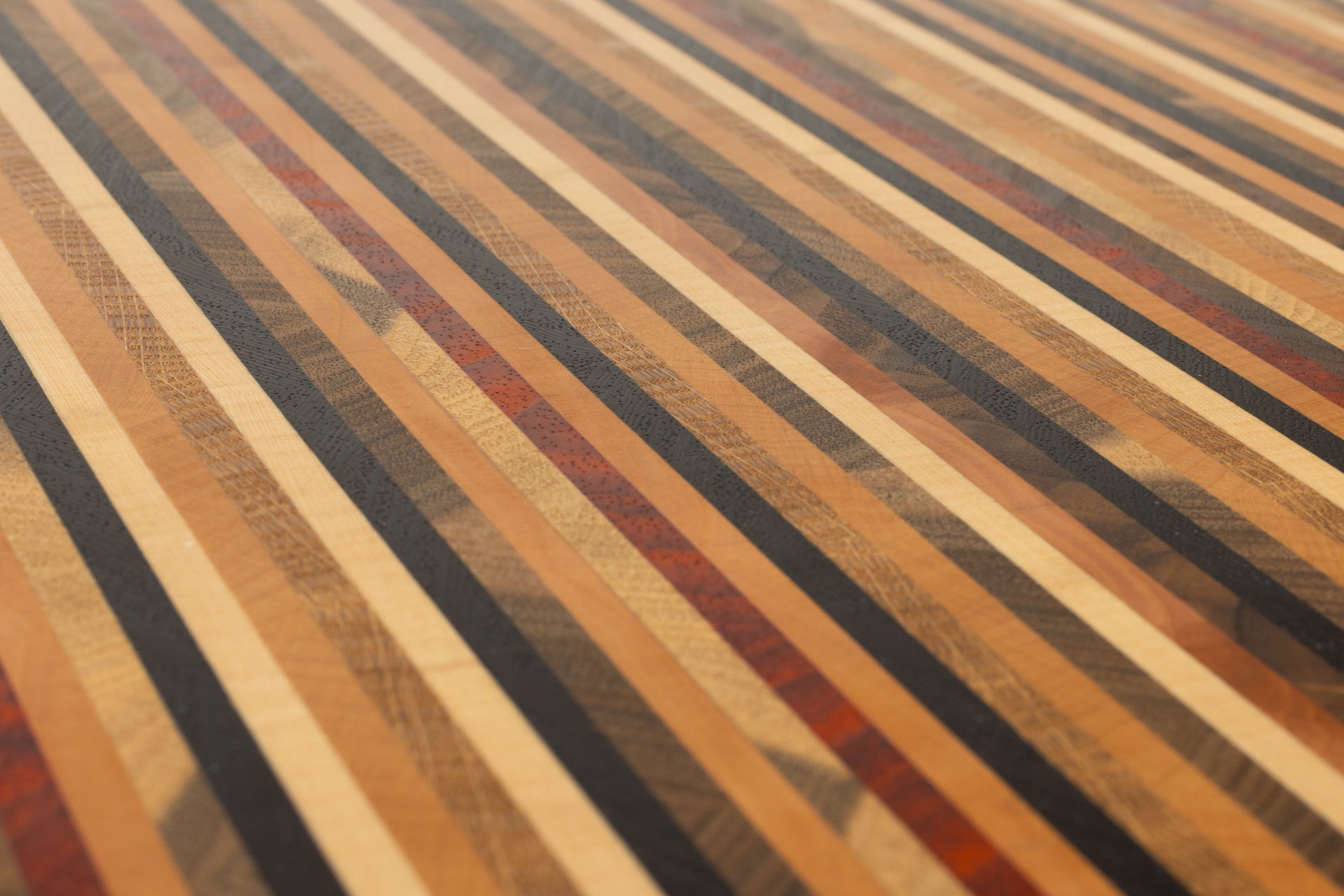 Gros plan sur le motif graphique multi-lignes de la planche à découper Signature, composée de 8 essences de bois précieux en bois de bout, fabrication artisanale française.