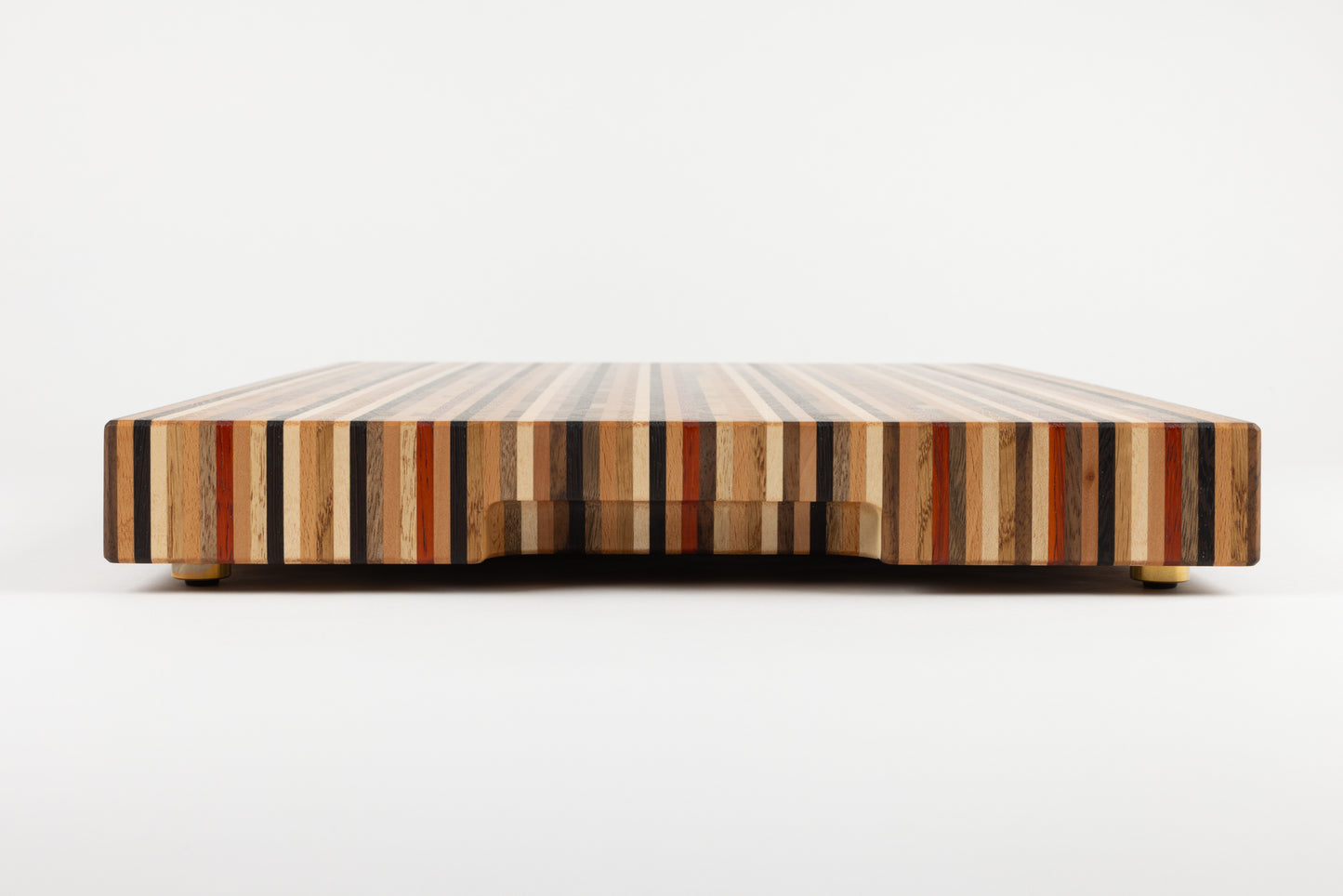 Planche à découper de luxe modèle Signature, vue latérale mettant en valeur ses pieds en laiton et son design en bois de bout réalisé avec 8 essences précieuses, fabrication française.