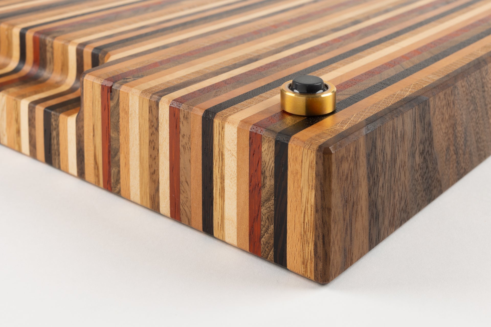 Détail rapproché d’une planche à découper Signature, pied en laiton massif avec patin antidérapant premium et arêtes finement biseautées, fabrication artisanale Made in France par un artisan d’art.