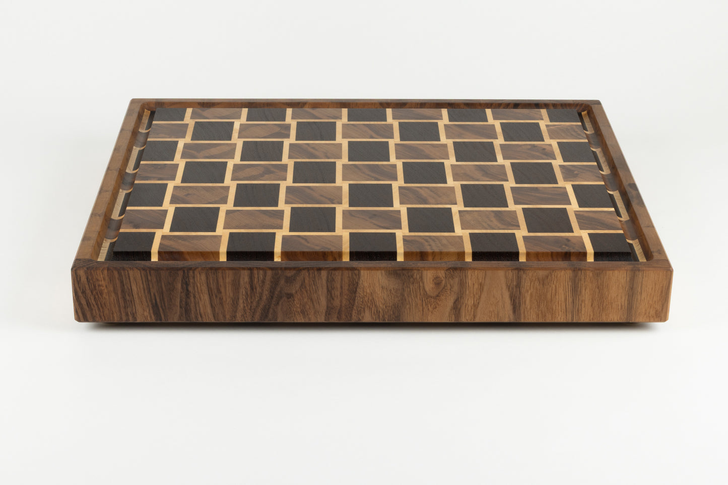 Vue de face d’une planche à découper artisanale, bordure élégante en noyer américain et motif damier en wengé, érable et noyer, réalisé en bois de bout.