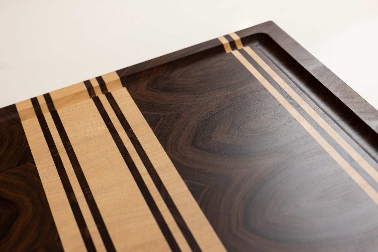 Gros plan sur une planche à découper de luxe en bois massif noyer américain, qualité haut de gamme des finitions et rigole à jus soignée, création artisanale Made in France