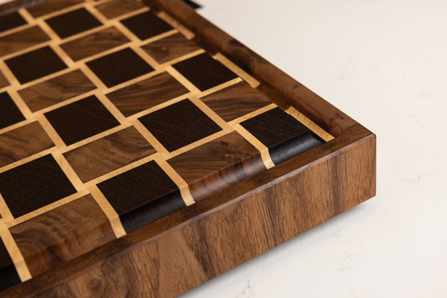 Planche à découper haut de gamme en bois de bout, photo du coin avec rigole à jus et finition polie lustrée, réalisée en essences nobles noyer américain, wengé et érable.