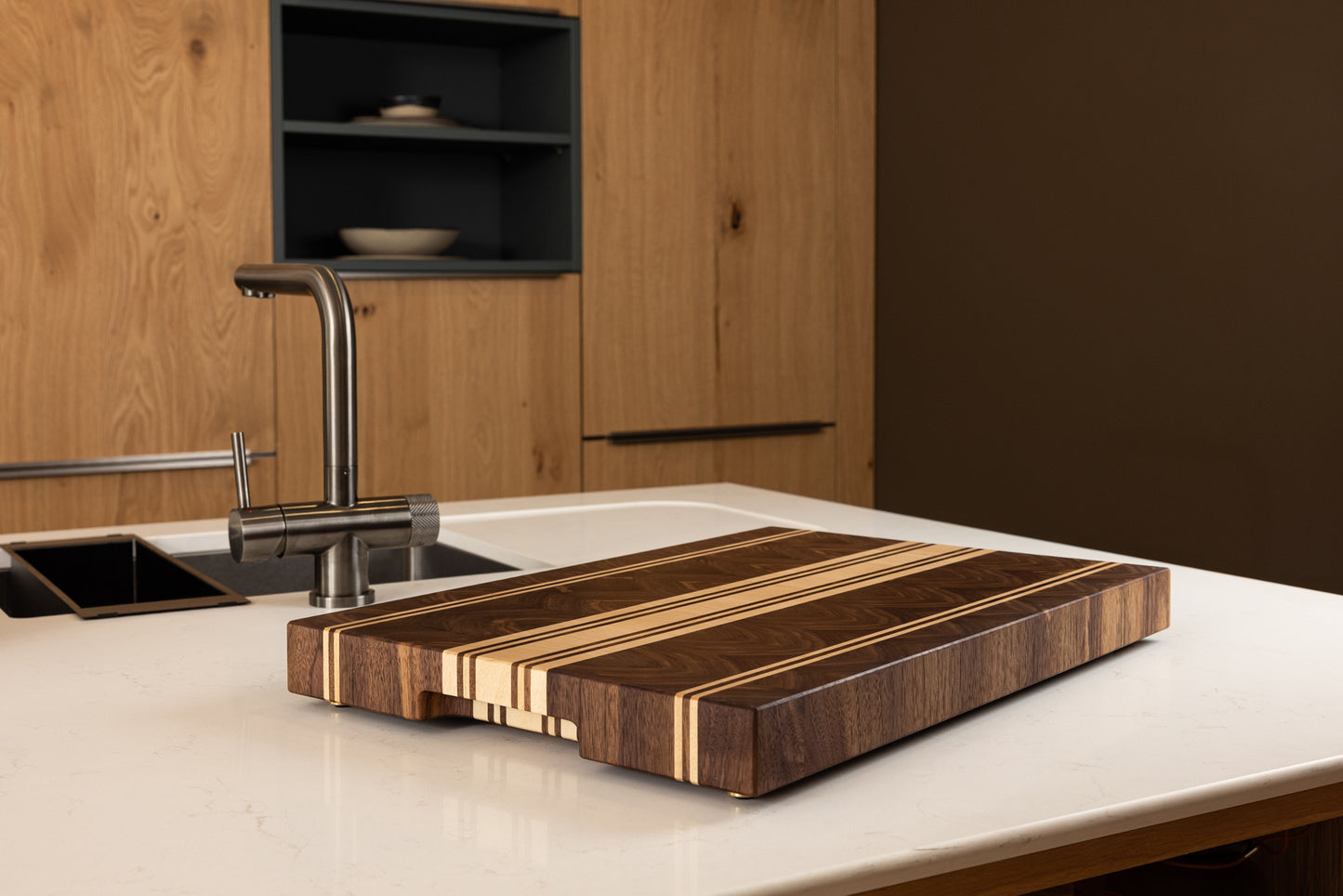 Planche à découper de luxe en bois massif multi-essences, version sans rigole à jus, présentée sur plan de travail en chêne dans une cuisine moderne, création artisan d’art Made in France.