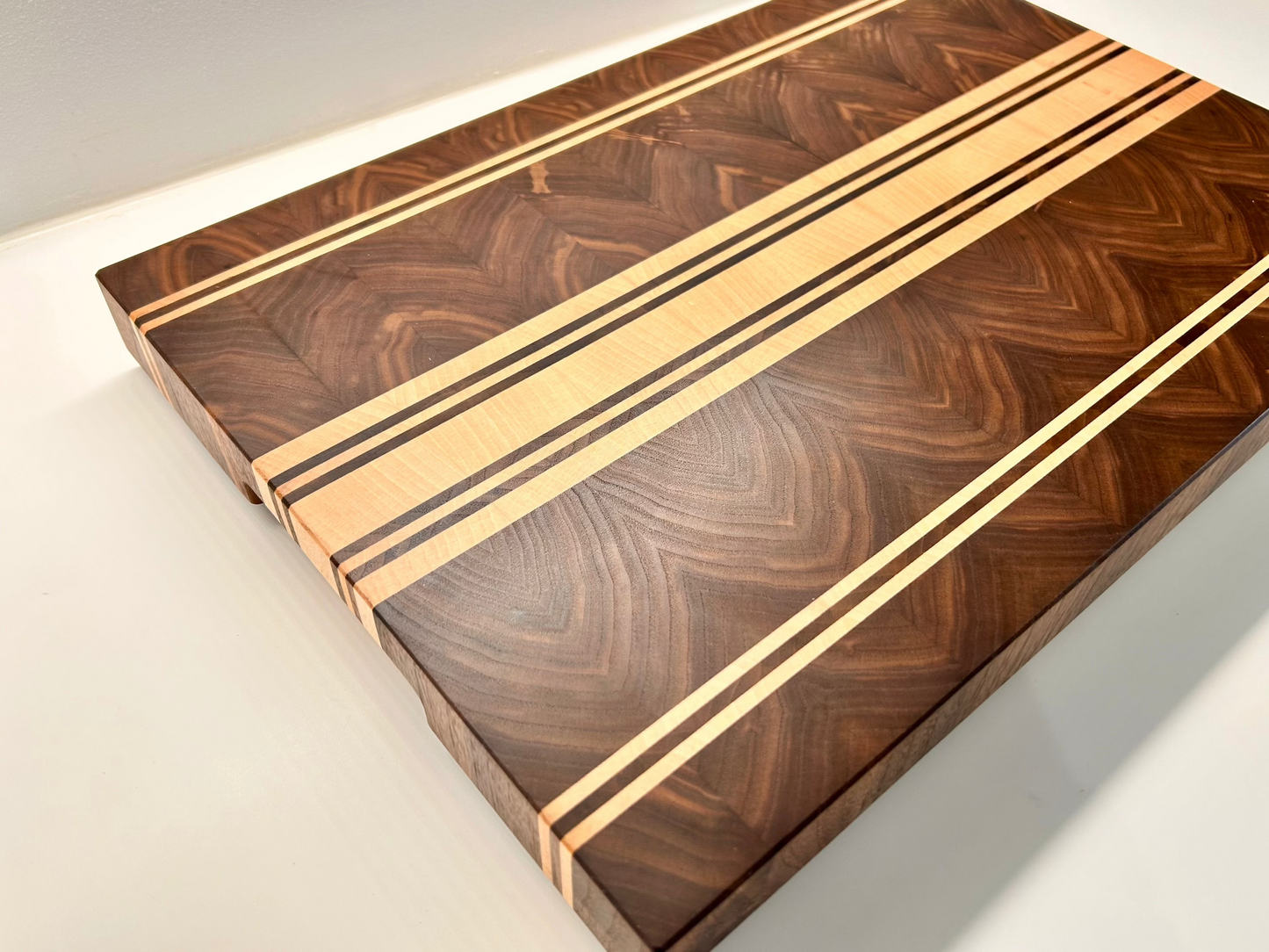 Vue de trois quart sur une planche à découper de luxe en noyer américain et érable, finition haut de gamme, fabriquée en France