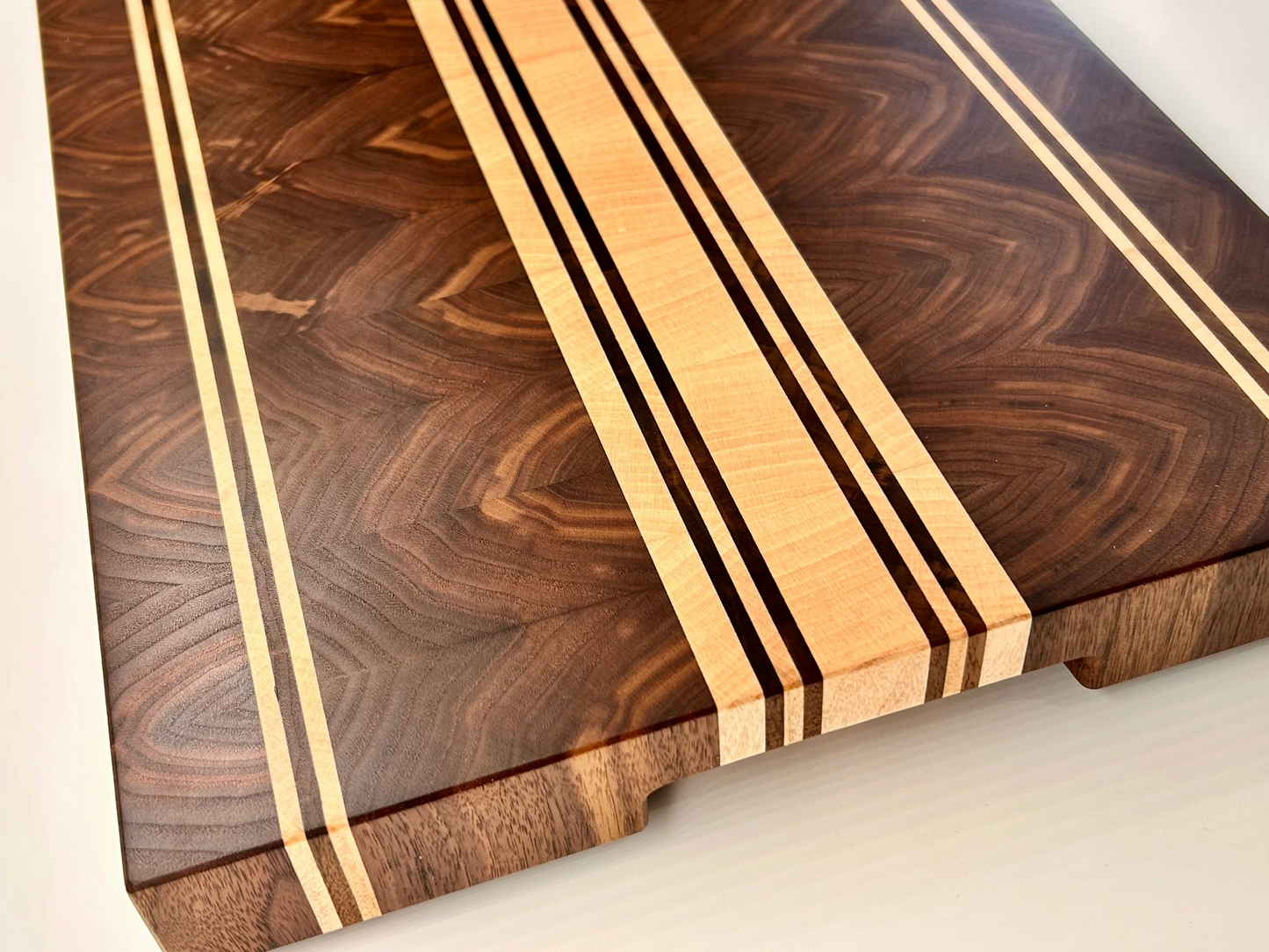 Vue de coté sur une planche à découper artisanale en noyer amériain et érable, surface lisse et finement lustrée, sans rigole à jus