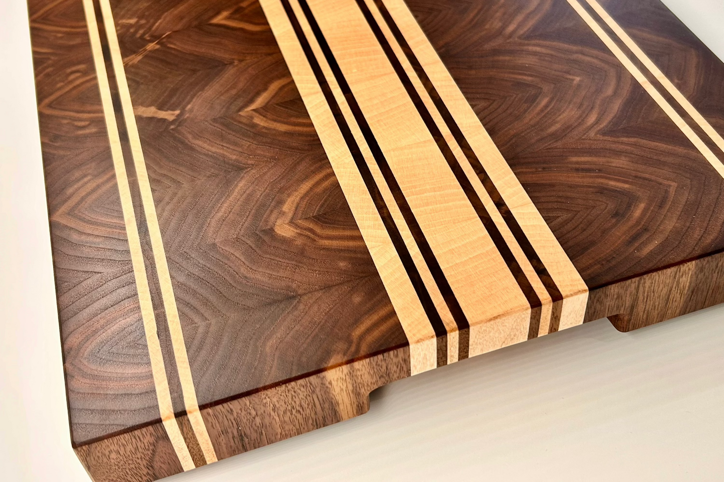 Vue de coté sur une planche à découper artisanale en noyer amériain et érable, surface lisse et finement lustrée, sans rigole à jus