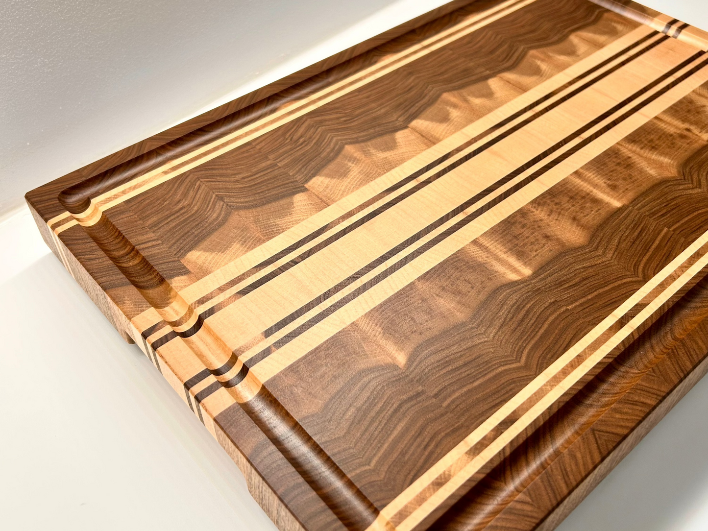 Vue de trois quart sur une planche à découper en noyer français et érable, finition premium à la cire d'abeille.