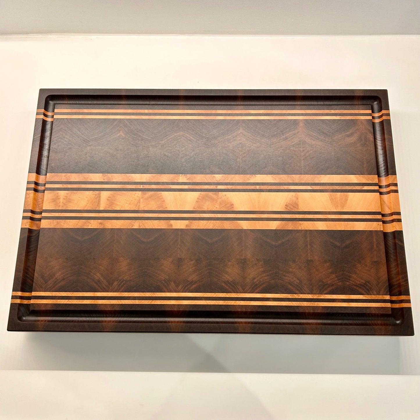 Vue de dessus de la planche à découper Debussy en bois de bout, réalisée en noyer et érable. Disposition des cernes en miroir mettant en valeurs le veinage
