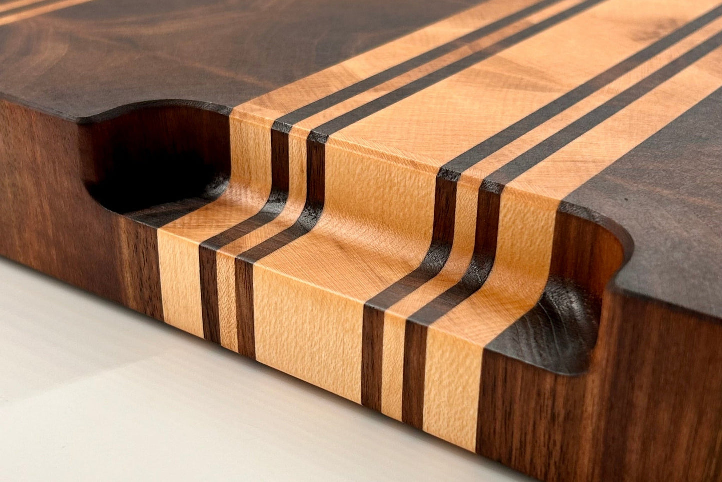 Détail de la poignée aux courbes douces et finition haut de gamme de la planche à découper Debussy en bois de bout, réalisée en noyer et érable.