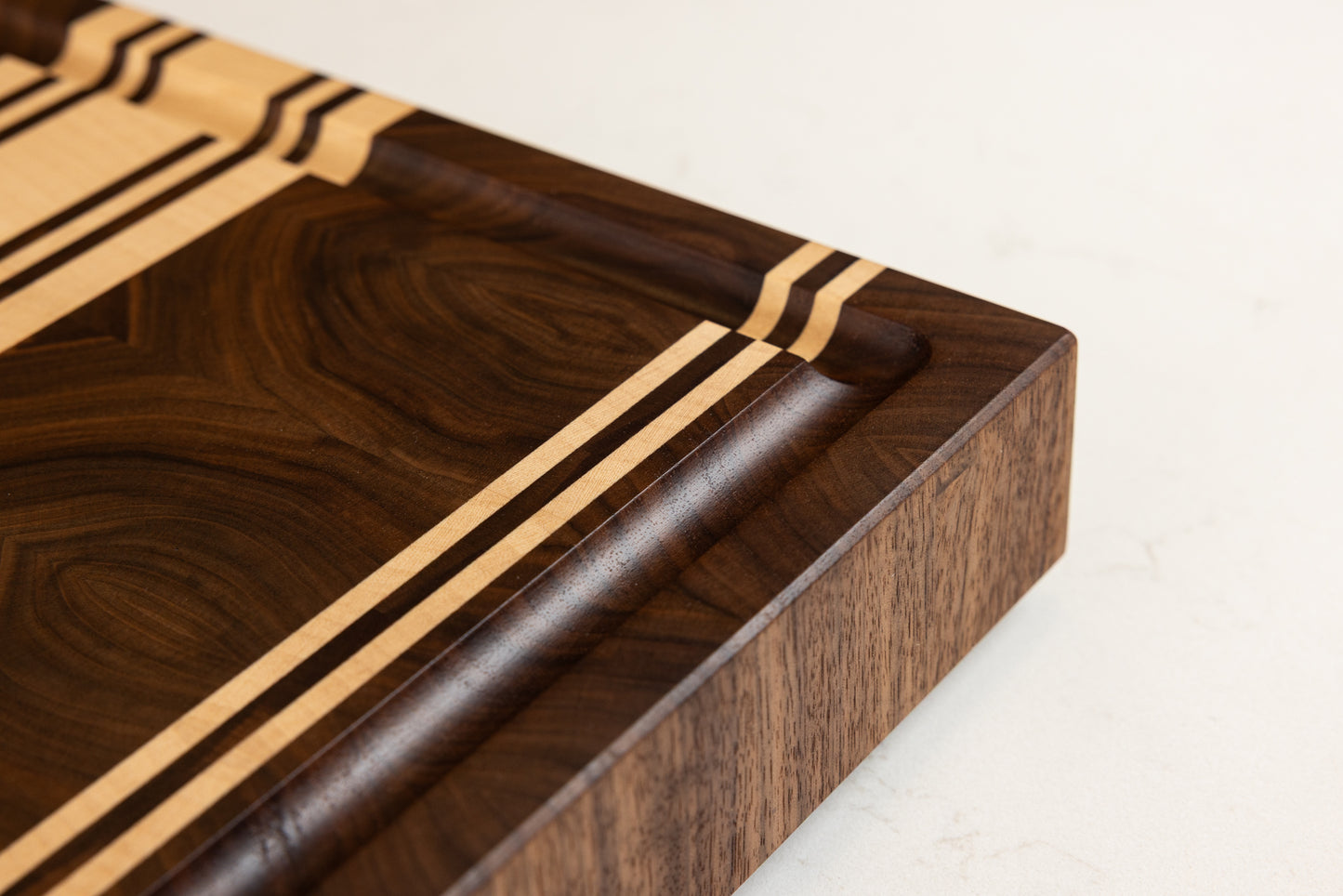 Vue rapprochée sur les finitions haut de gamme d’une planche à découper artisanale en noyer américain et érable, arêtes finement biseautées et travail d’artisan d’art français.